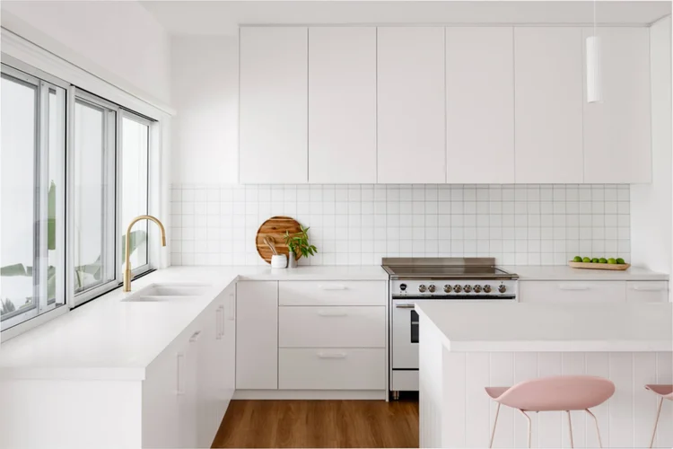 White kitchen with gold tapware, a tiled splashback and a freestanding oven at the Warilla Beach House