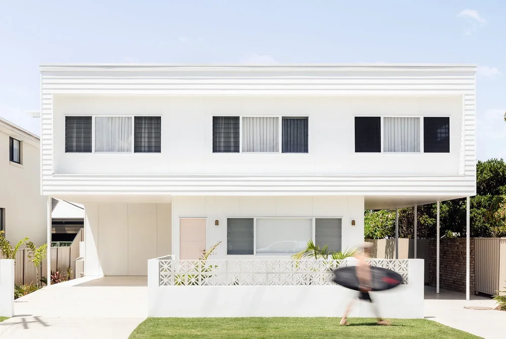 Warilla Beach House by CKS Projects: a white two-storey home with a breeze-block front fence and lawn