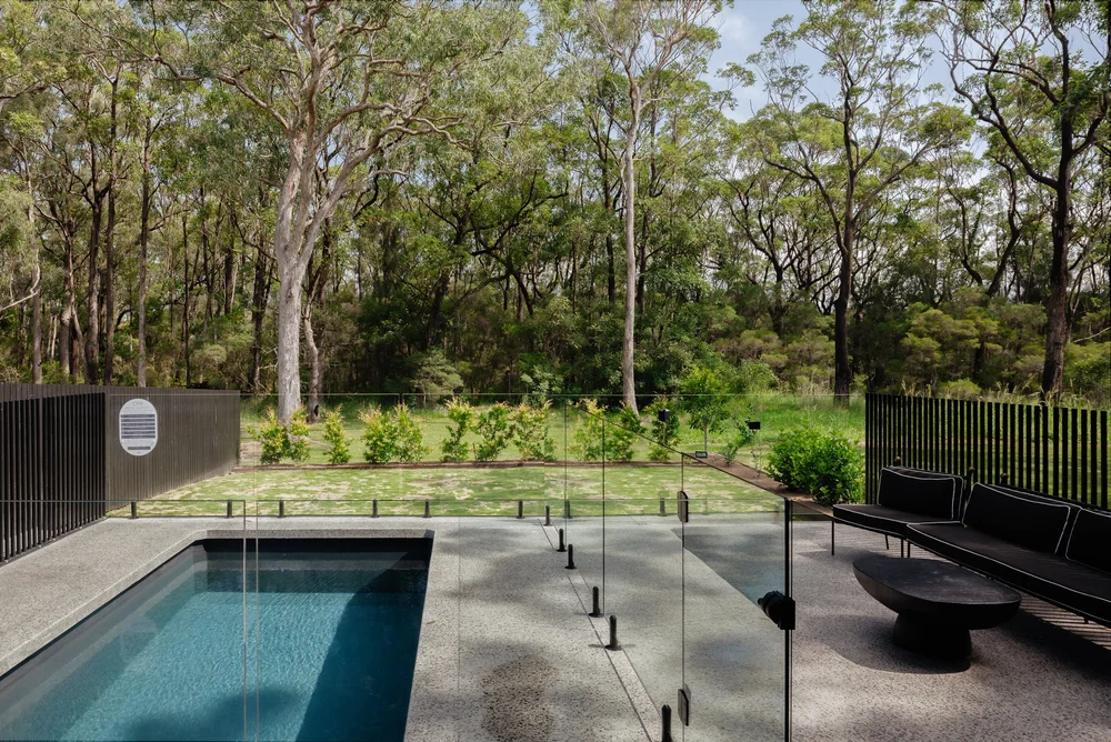 Plunge pool with glass fencing, concrete paving and new lawn against tall eucalypt bushland at the Huskisson Duplex by CKS Projects