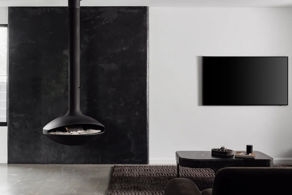 Suspended black fireplace against a dark feature wall in the living room of the Huskisson Duplex by CKS Projects