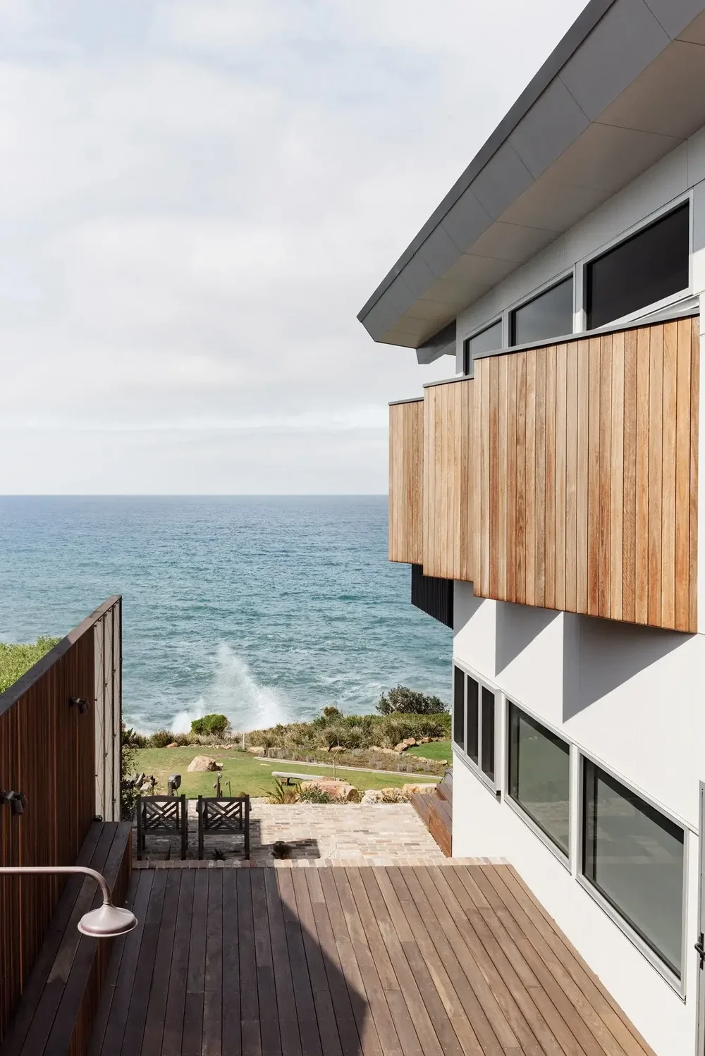 Timber-clad upper level and deck looking over the ocean at Wombarra Clifftops by CKS Projects