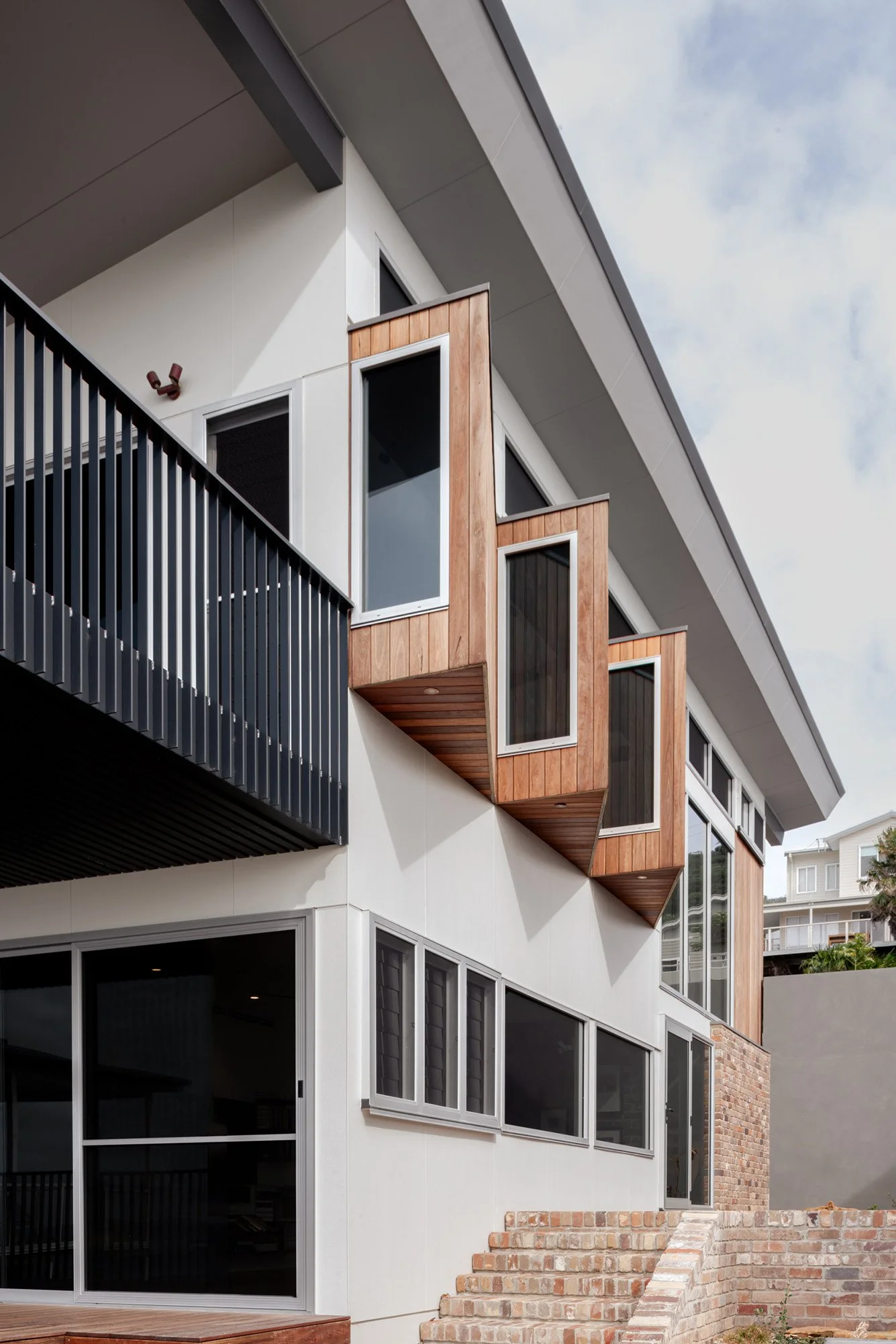 Wombarra Cliff Top by CKS Projects, with timber-clad bay windows, a black balcony and recycled brick steps