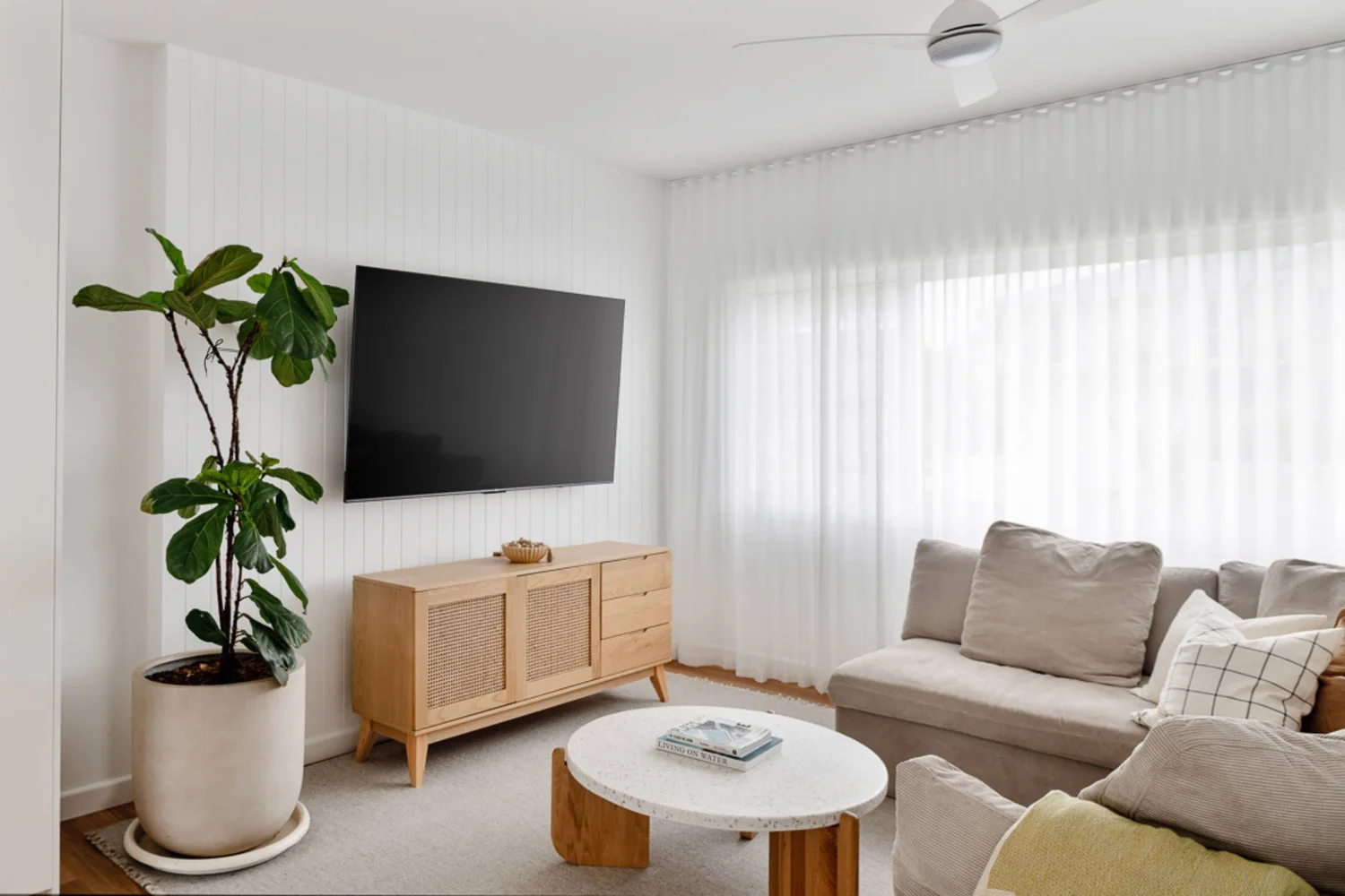 Light-filled living room with sheer curtains, oak flooring and a timber sideboard at the Warilla Beach House