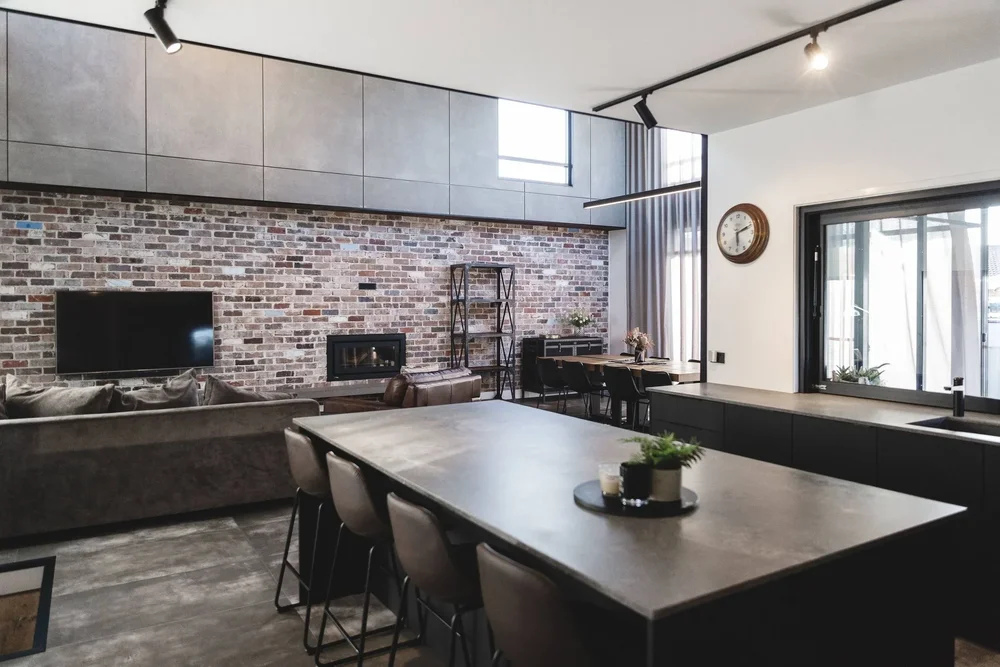 Living and dining room with a recycled brick feature wall, polished concrete floor and black dining table at Ocean Windang by CKS Projects