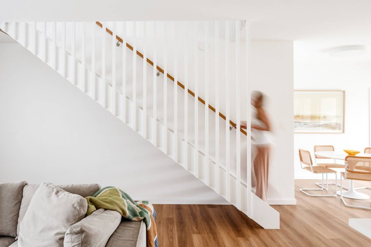Open white staircase with a timber handrail rising from the living area to the first-floor addition at the Warilla Beach House