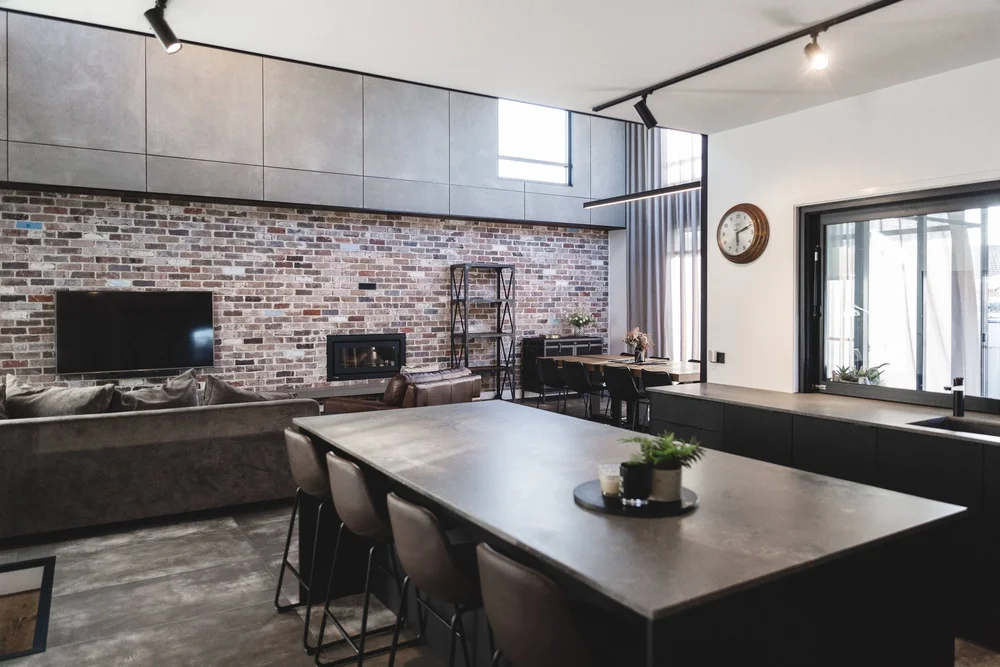High-ceilinged living and dining area with a brick feature wall in the Ocean Windang extension by CKS Projects
