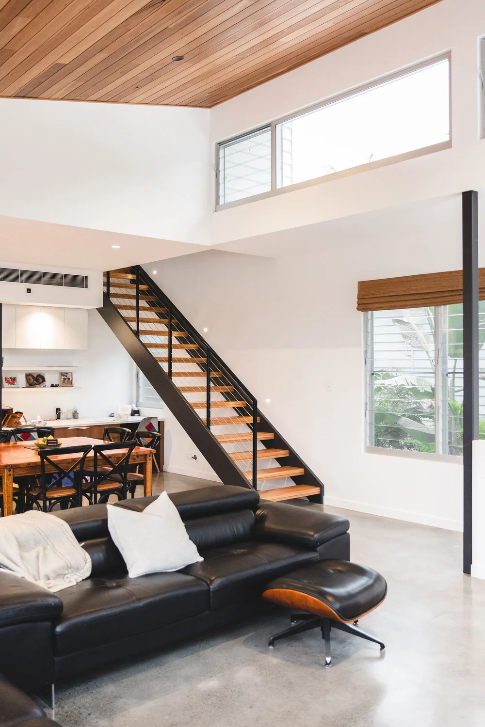 Open living area with a black steel stair, polished concrete floor and black leather sofa in a Woonona home by CKS Projects