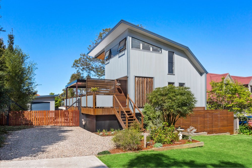 The Barn Woonona: barn-style home with raked roof and timber deck on a steep escarpment block, built by CKS Projects