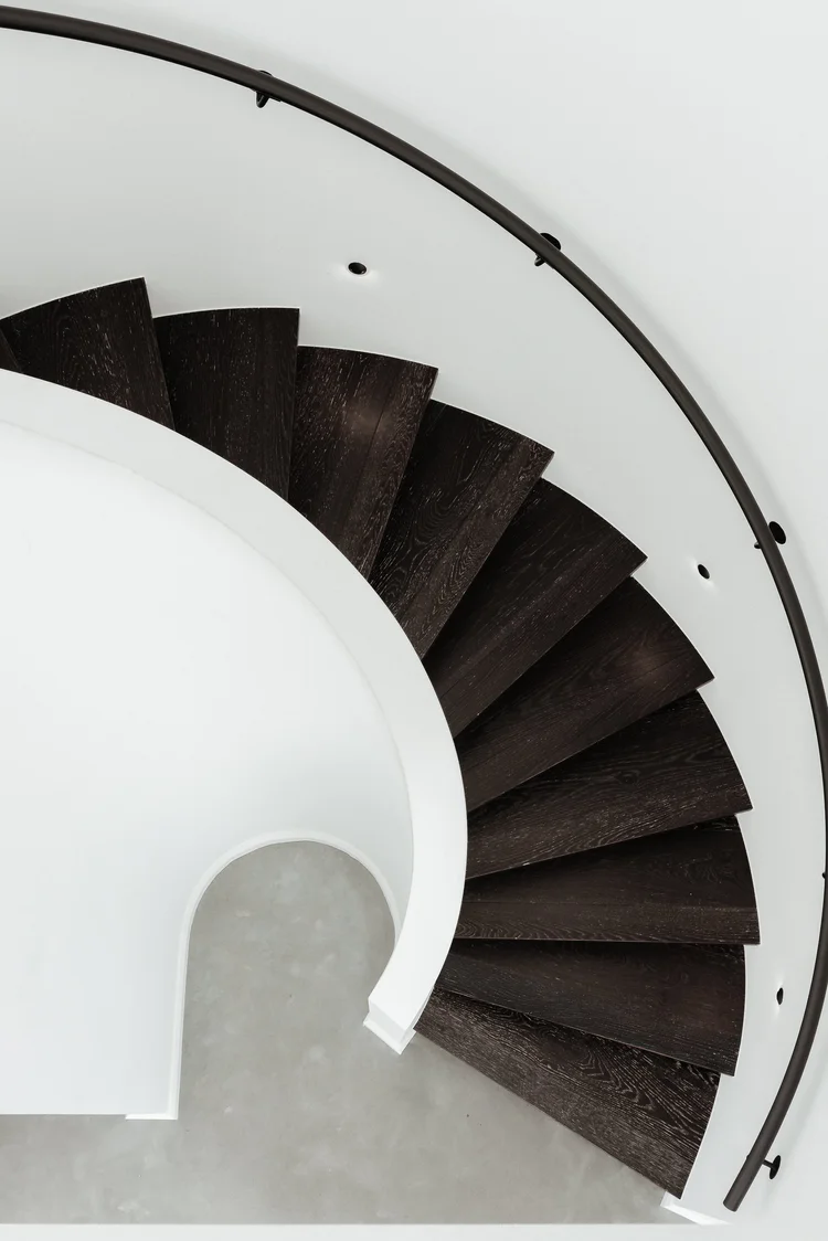 Dark timber spiral staircase curving between levels in the Huskisson project by CKS Projects