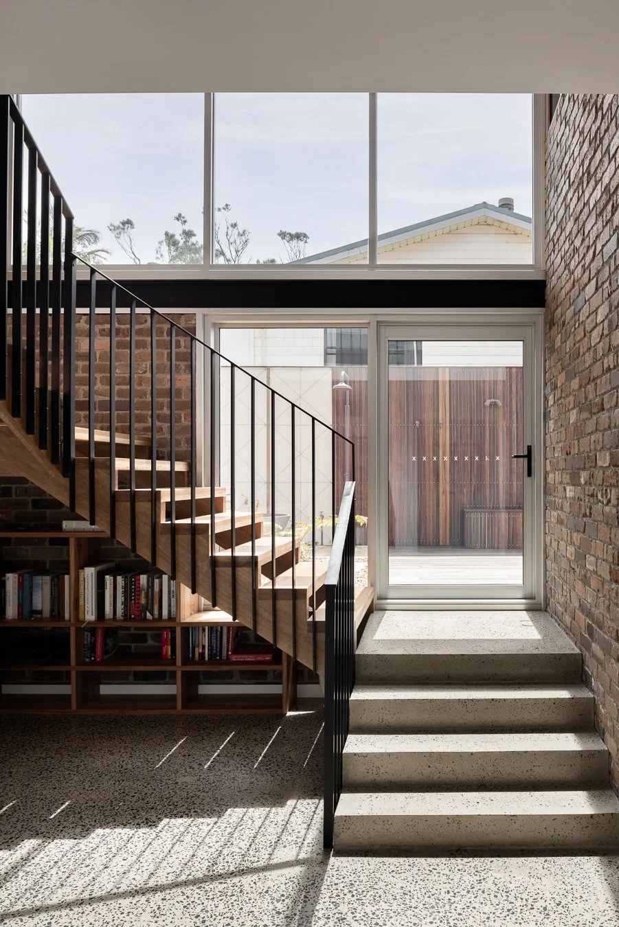 Timber stair with black steel balustrade beside a brick wall and polished concrete steps at Wombarra Clifftops by CKS Projects