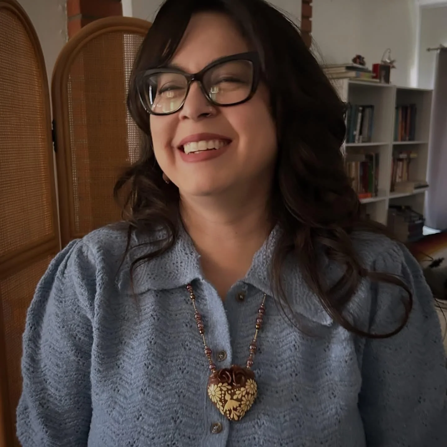 Irene Sanchez in a blue top and heart necklace smiling and looking to the side