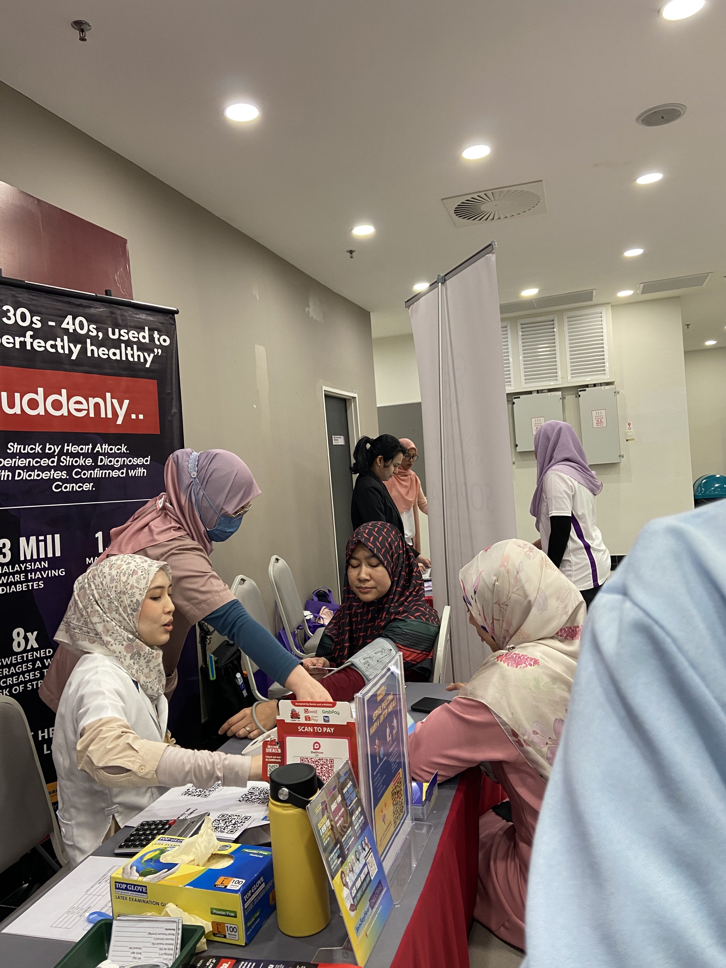 Healthcare workers or volunteers attending to patients or participants at a health-related event or clinic with informational posters and health supplies on the table.