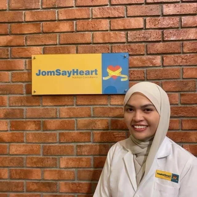 A young woman wearing a white medical coat and a dark hijab, smiling, against a plain white background.