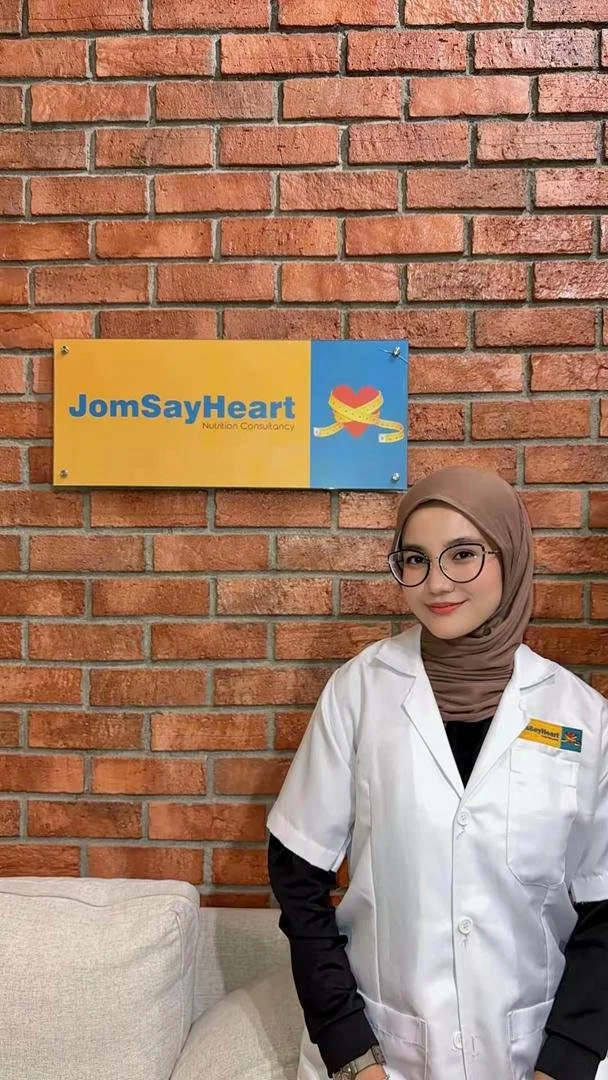 A young woman in a white medical uniform and hijab, standing against a plain white background.