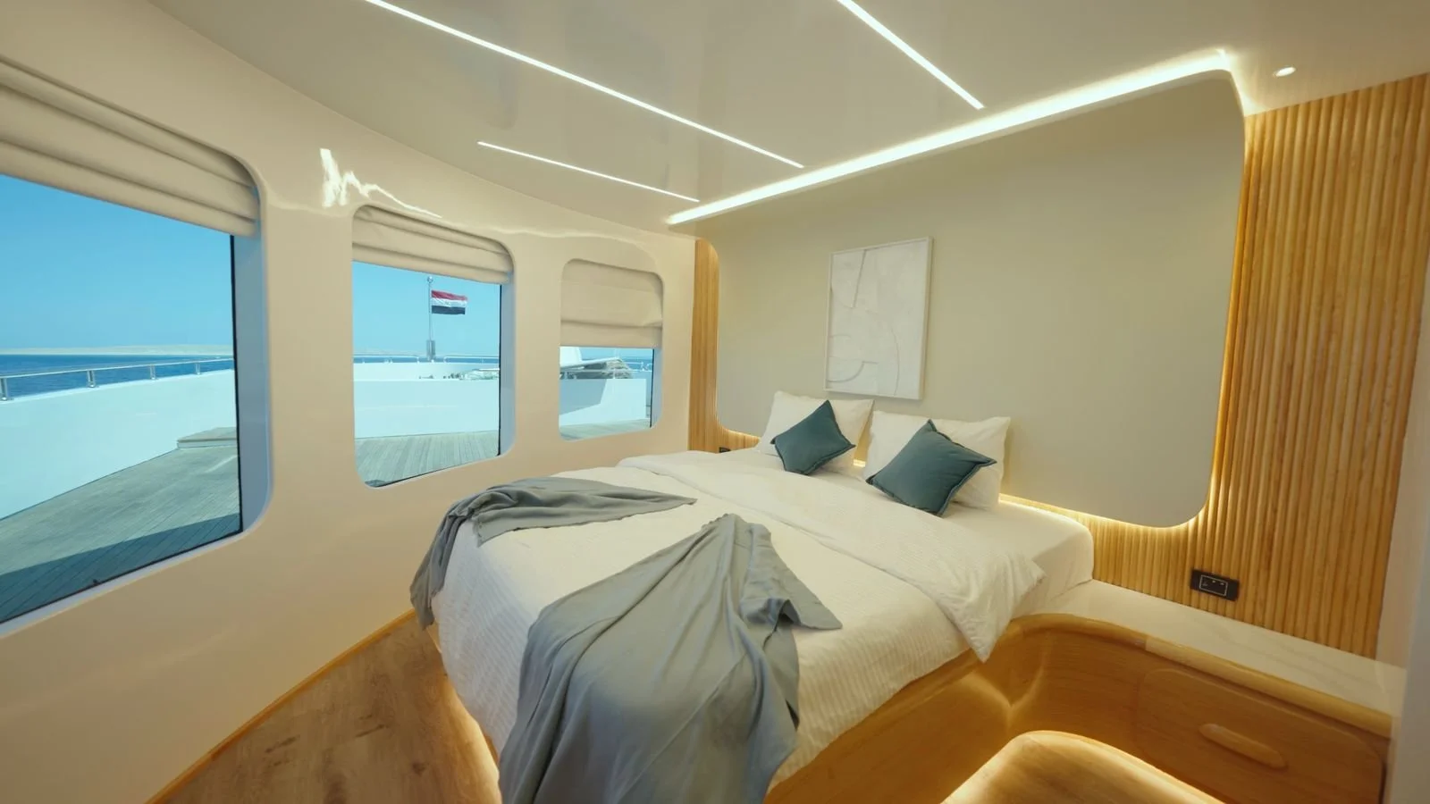 Modern bedroom with large windows showing a yacht and a flag outside, white walls, wooden accents, and a minimalist design.
