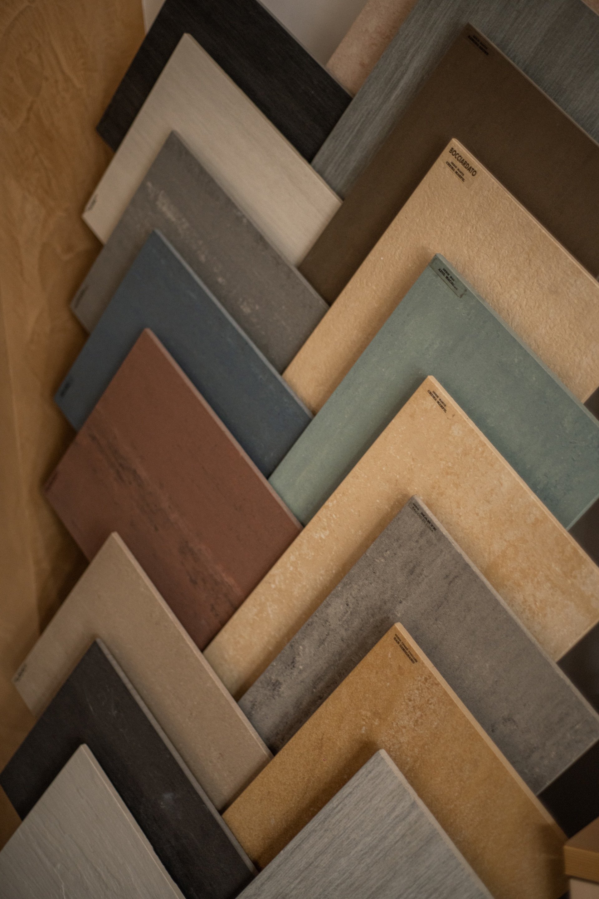 Campioni di vari colori e texture di piastrelle per pavimenti o rivestimenti esposti in un negozio, disposti in fila e visti di sghembo.