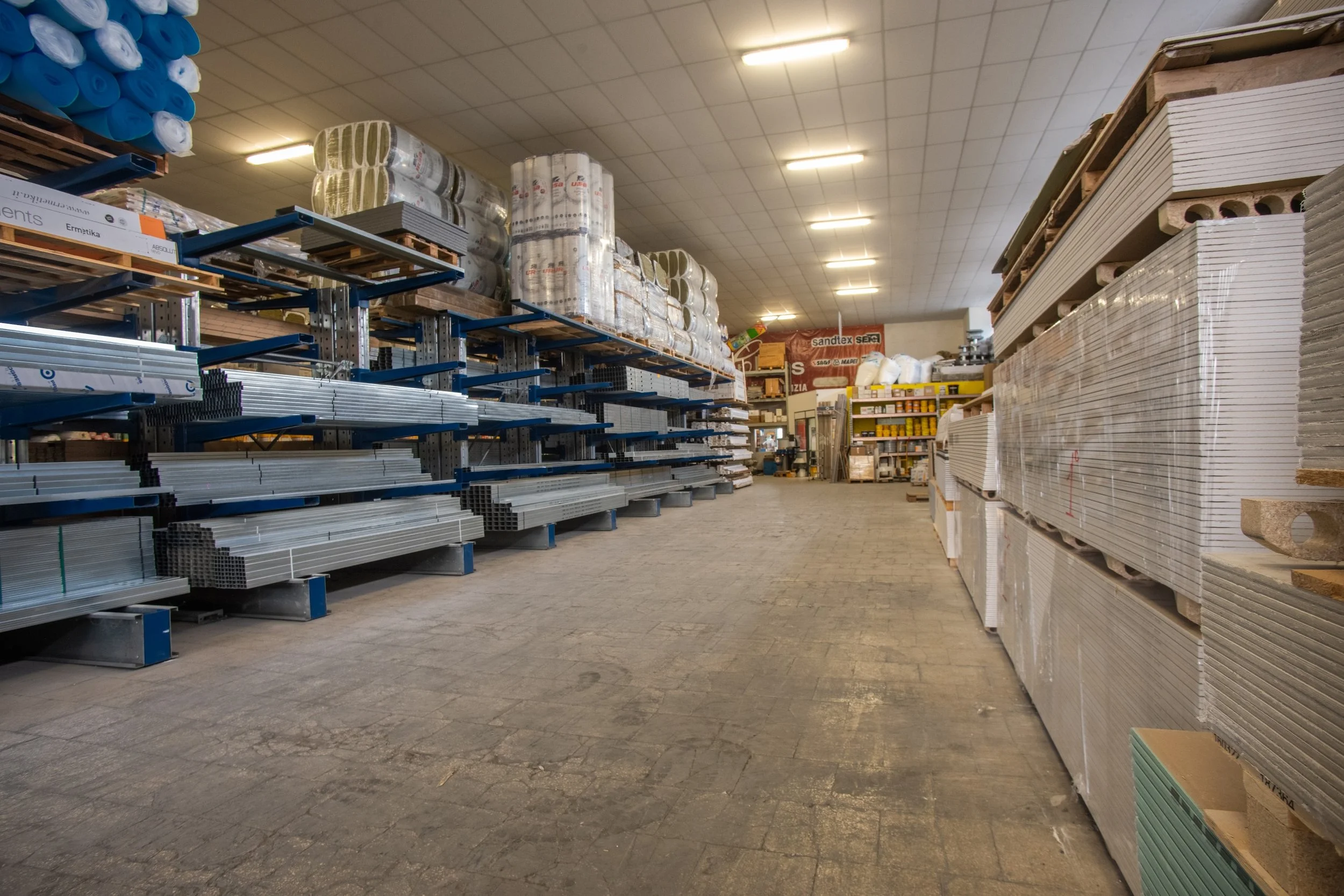 Scaffali di materiali edili in un negozio di ferramenta, con tubi di metallo, pannelli di cartongesso e altri materiali per edilizia.