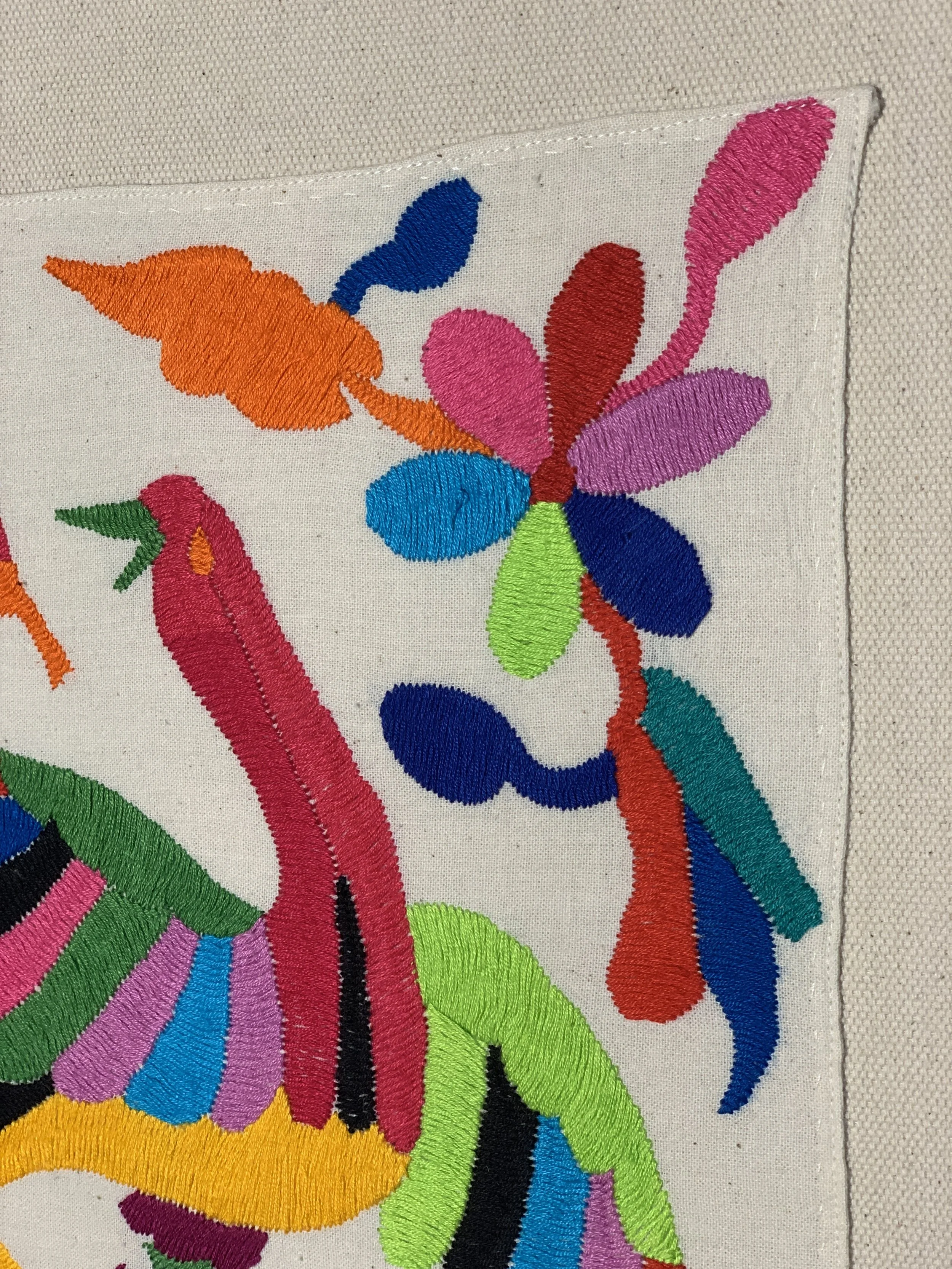 Bunt bestickter Stoff mit abstrakten Blumen- und Tiermustern in leuchtenden Farben wie Pink, Blau, Grün, Orange und Schwarz.