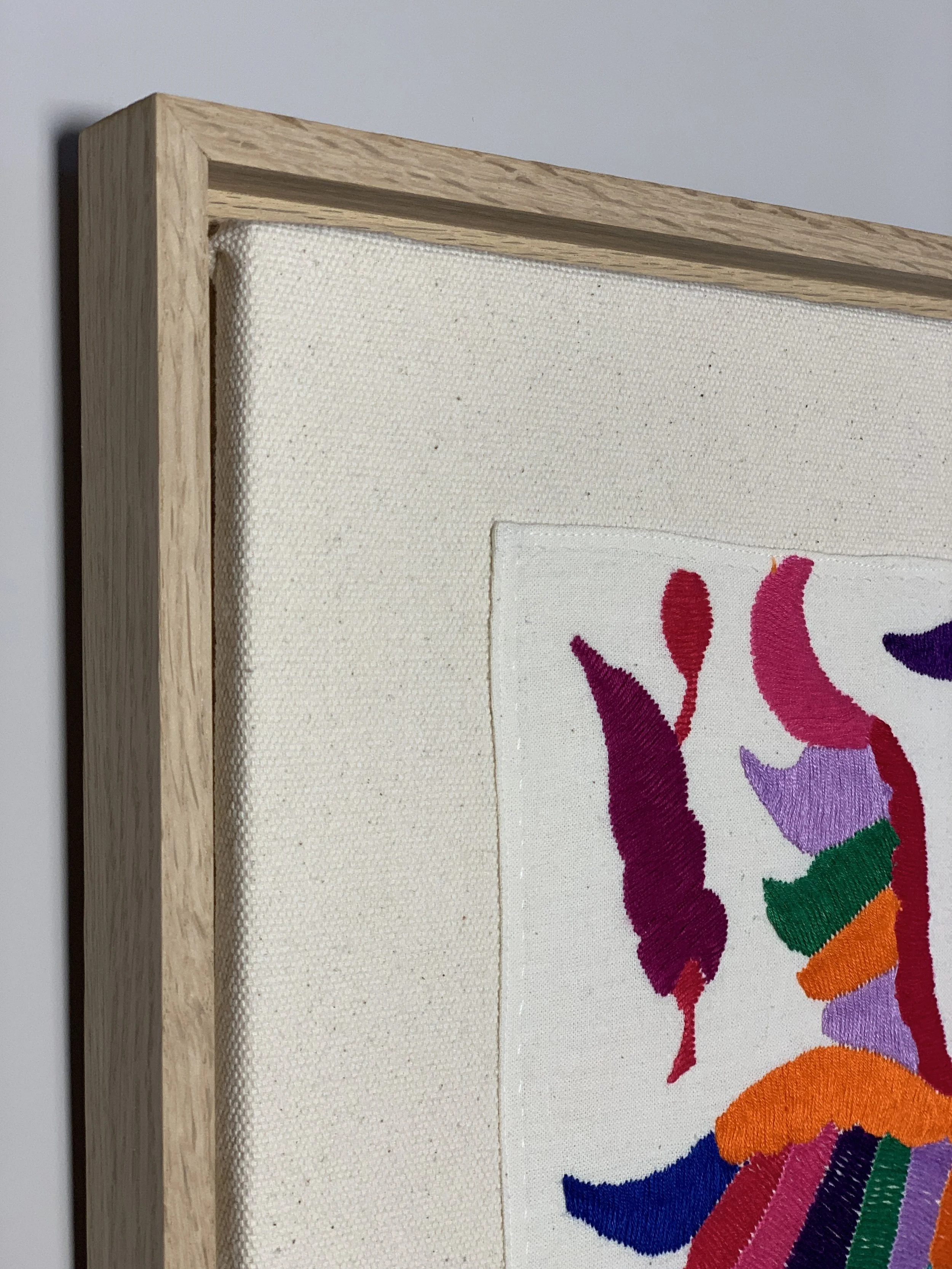 Nähe eines gebundenen Stoffbildes mit buntem, abstraktem Stickmuster in einem Holzrahmen