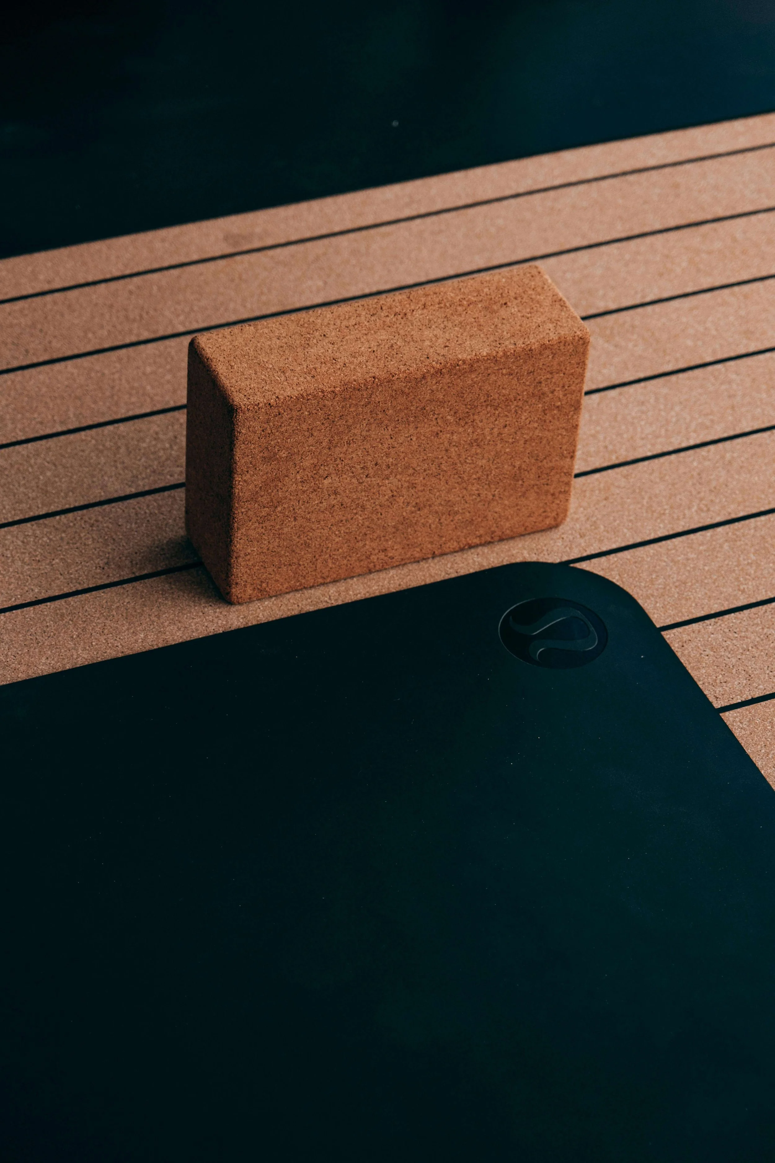 A brown brick resting on a brown textured mat with black lined lines, with part of a black object visible in the lower right corner.