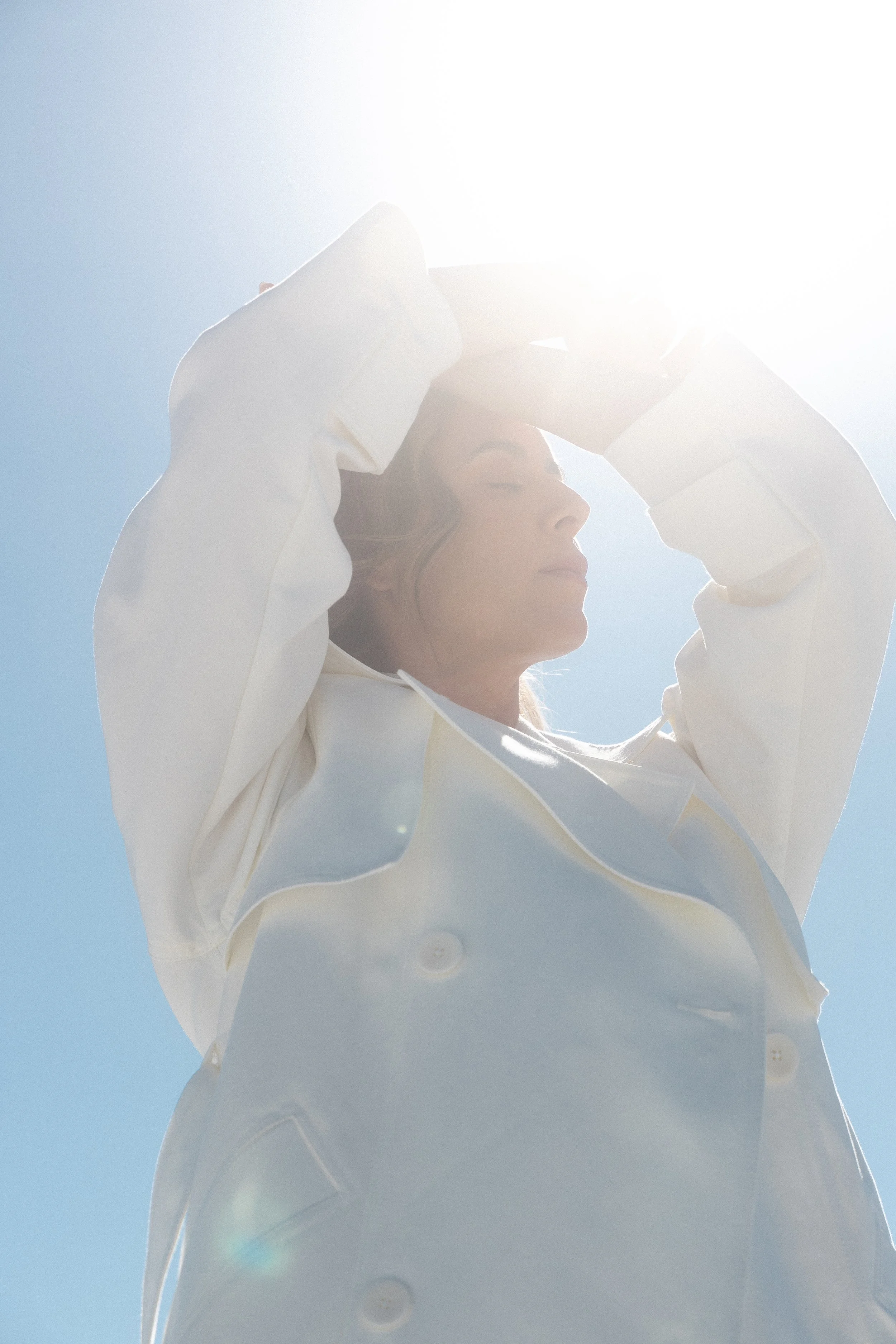 Pessoa com roupa branca de olhos fechados contra o sol.