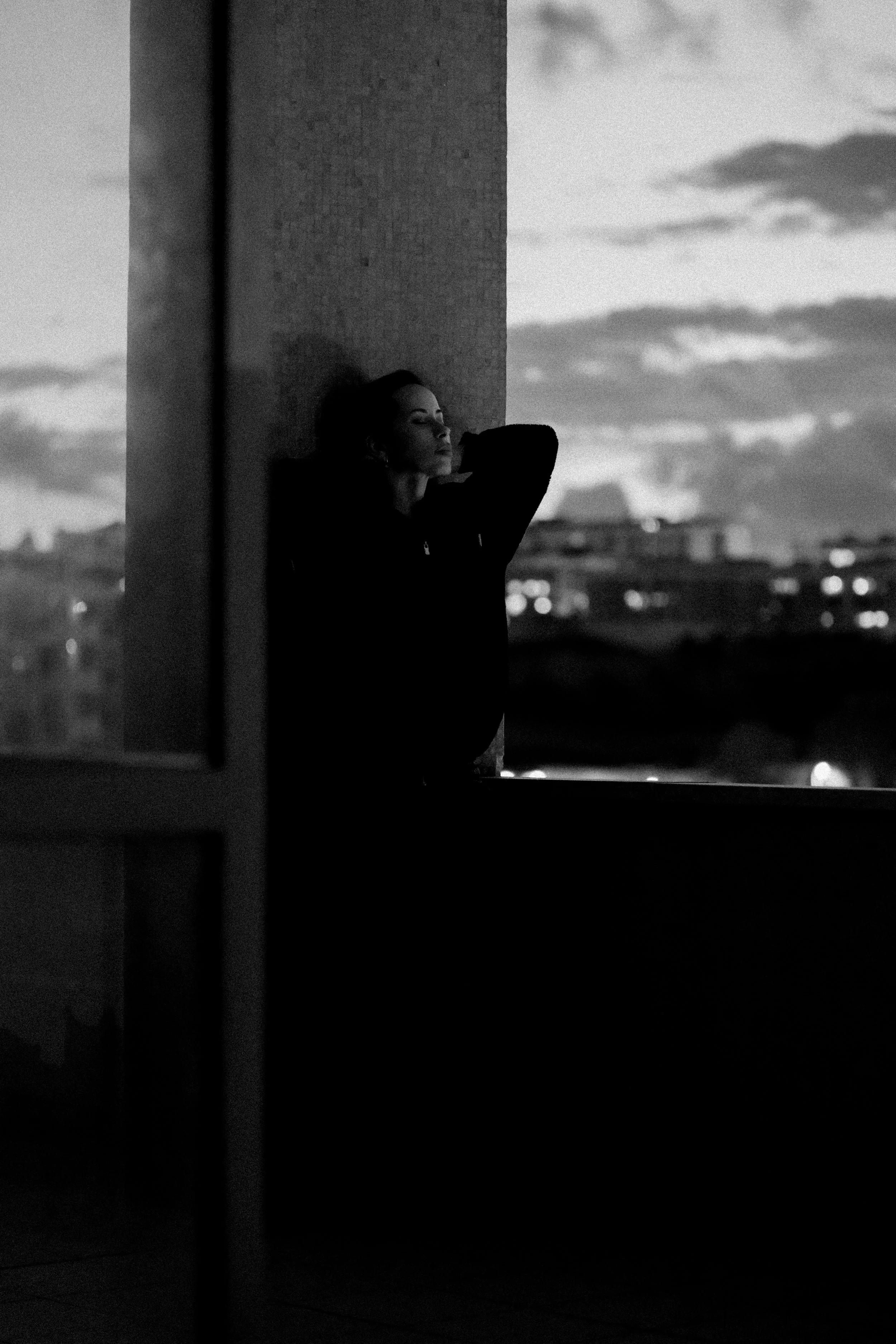 Pessoa encostada em pilastra ao anoitecer, em preto e branco.