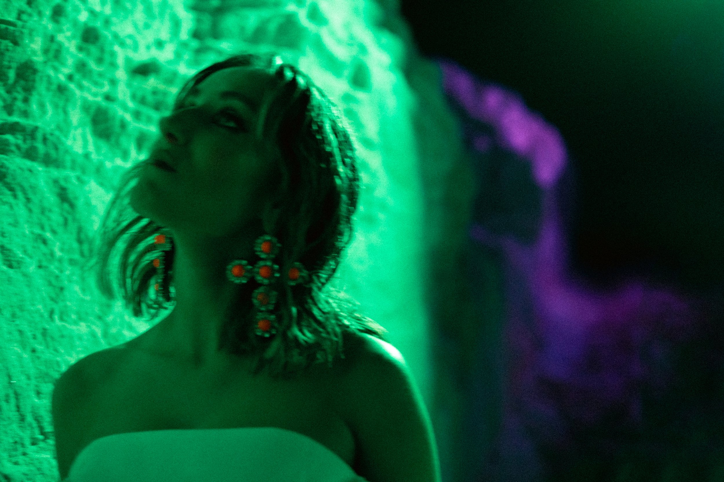 Mulher com brincos grandes em luz verde e roxa, de noite.