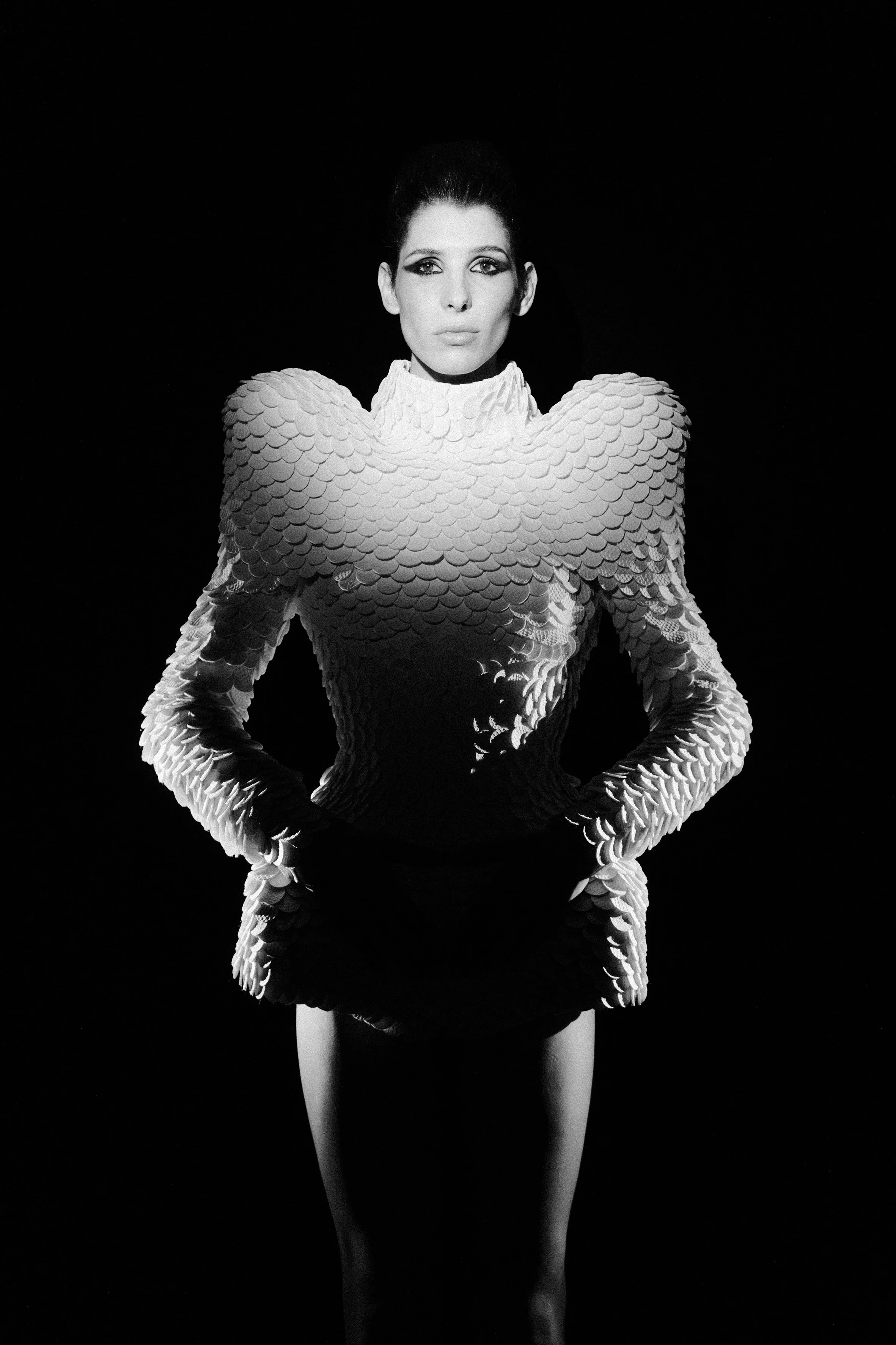 Mulher em traje futurista com textura de escamas, fundo escuro.