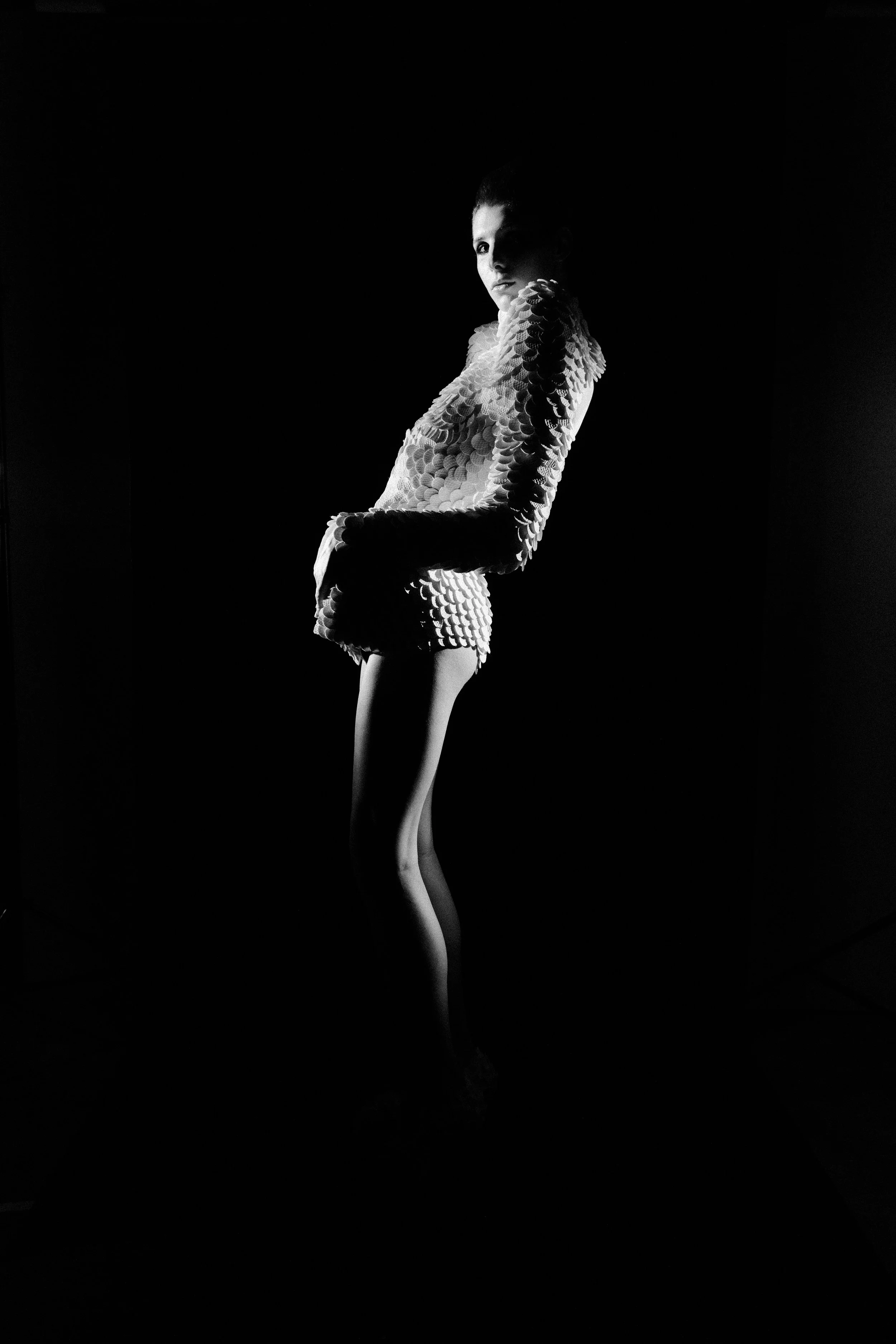 Figura feminina em traje de textura única, posando artisticamente em iluminação dramática, preto e branco.