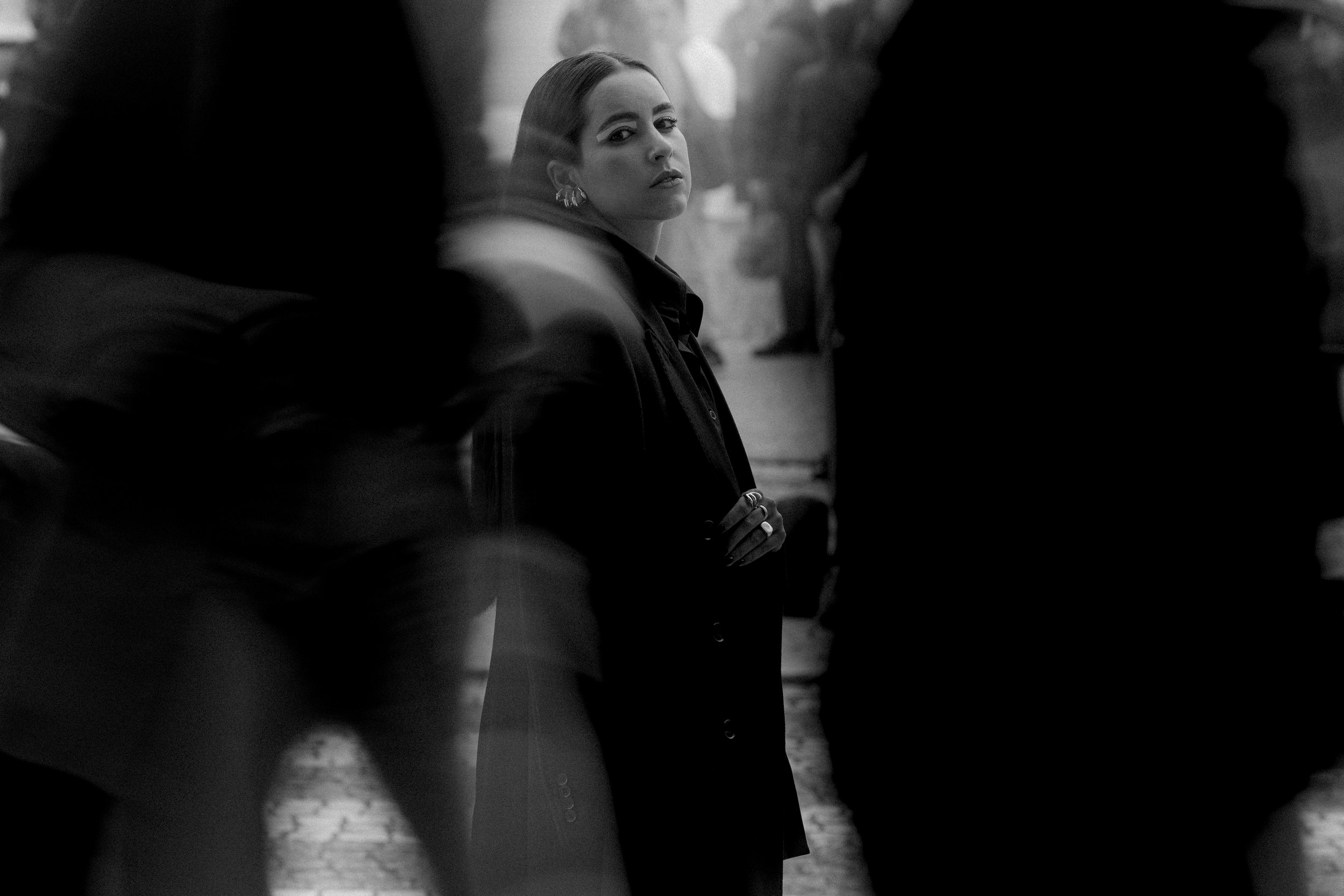 Mulher em pé na rua rodeada por pessoas em movimento, imagem em preto e branco, expressando contraste entre foco e borrão.