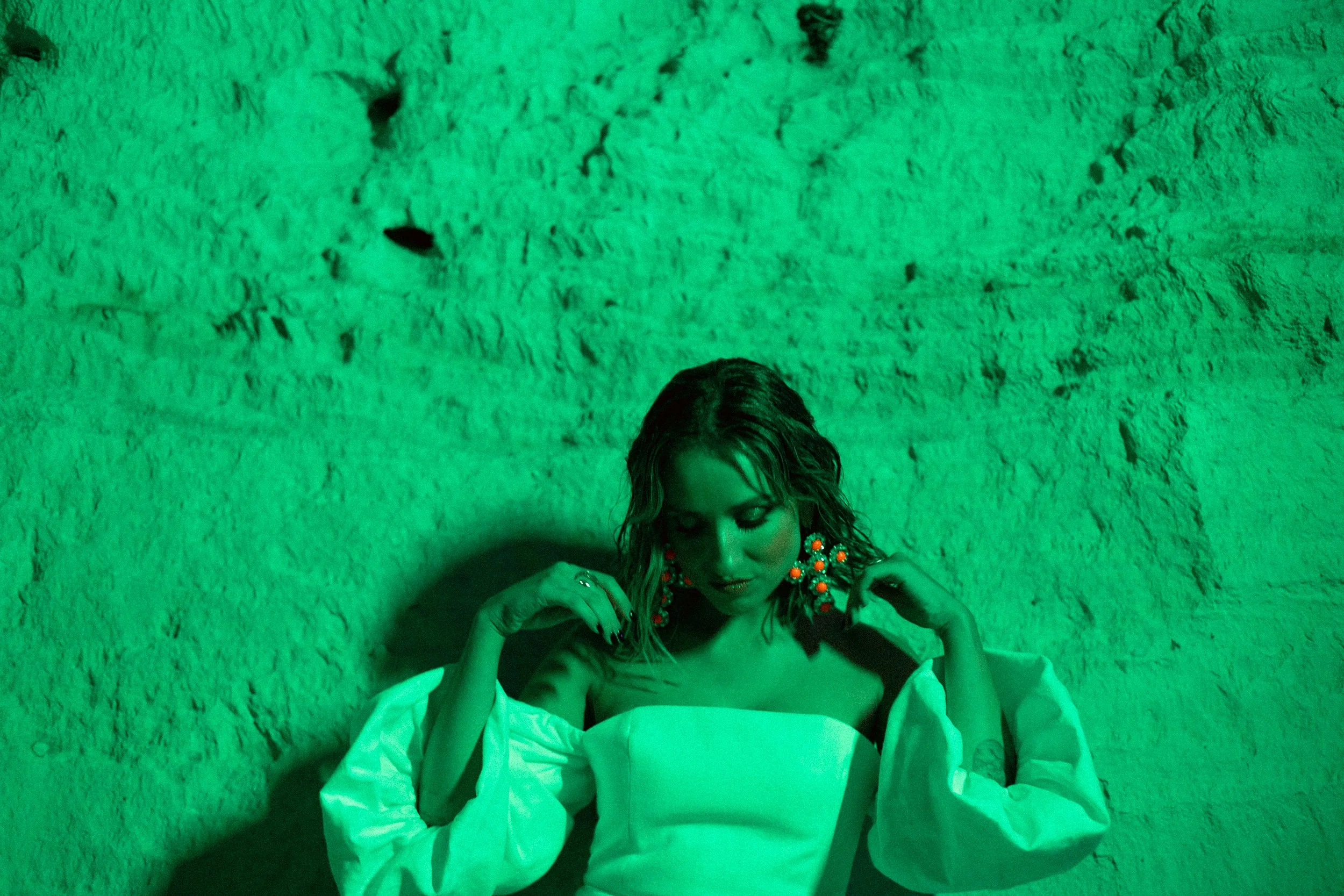 Mulher em roupa elegante com iluminação verde, fundo texturizado.