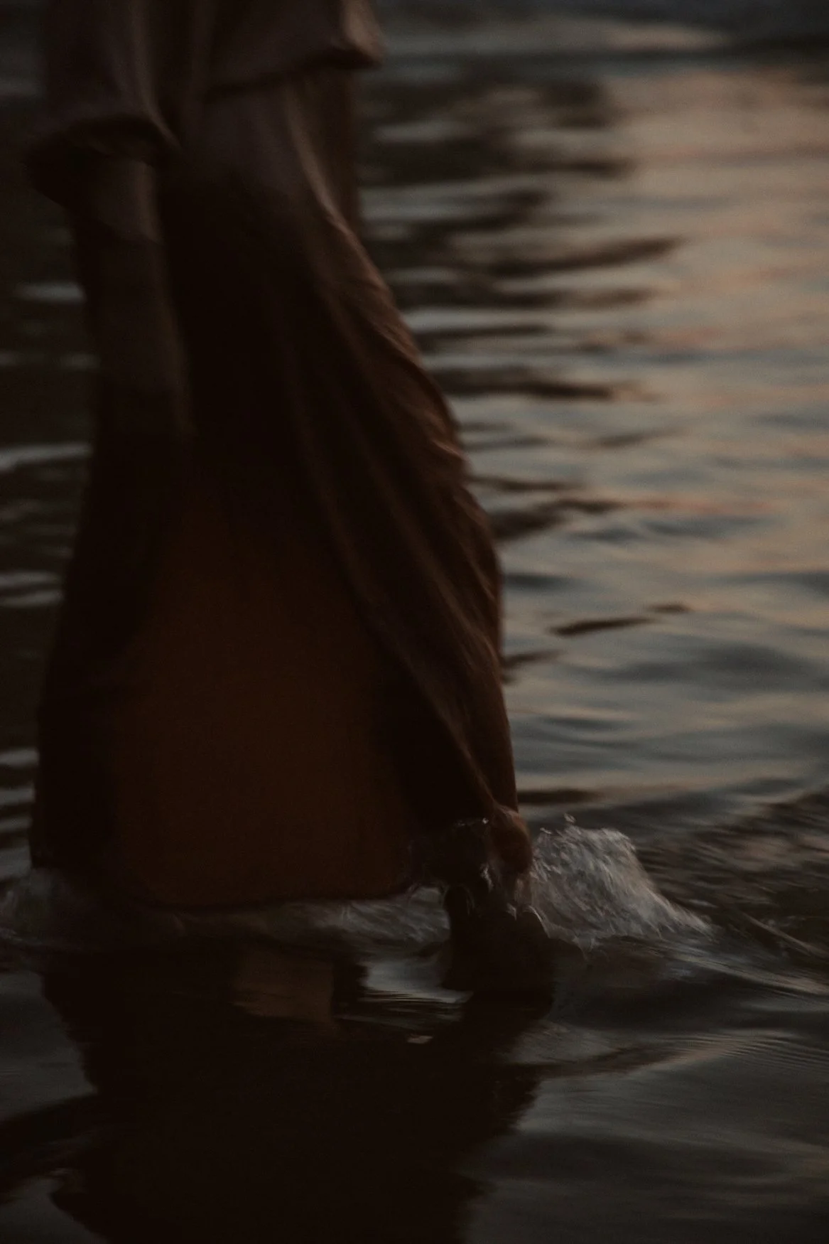 Pessoa caminhando em águas rasas ao amanhecer ou entardecer, com vestido longo.