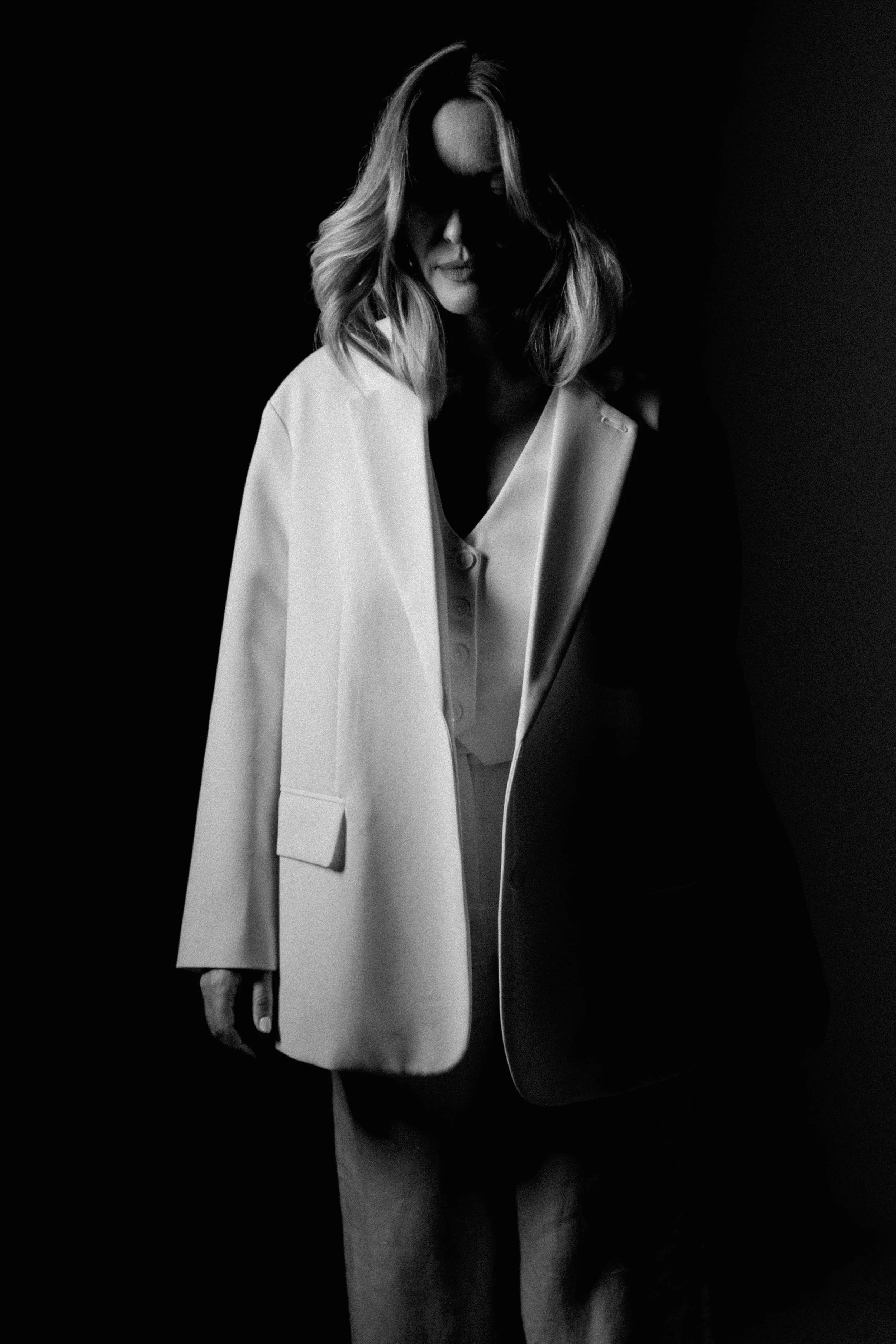 Mulher em preto e branco vestindo um blazer claro, parcialmente envolta em sombras.