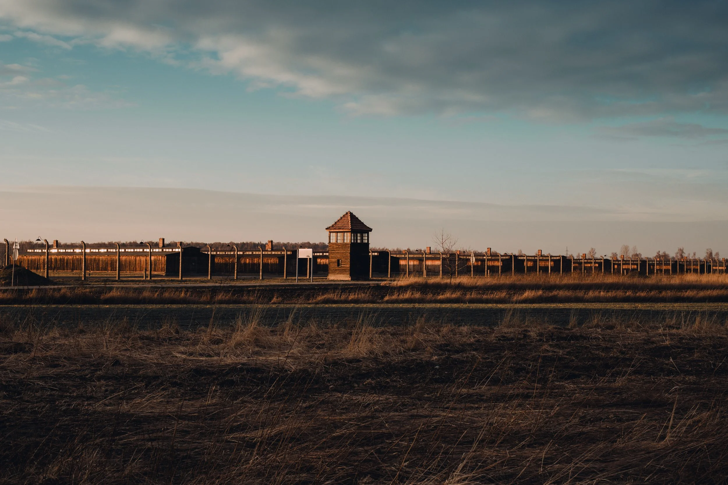 Campo cercado com uma torre de vigia ao centro, sob um céu parcialmente nublado.