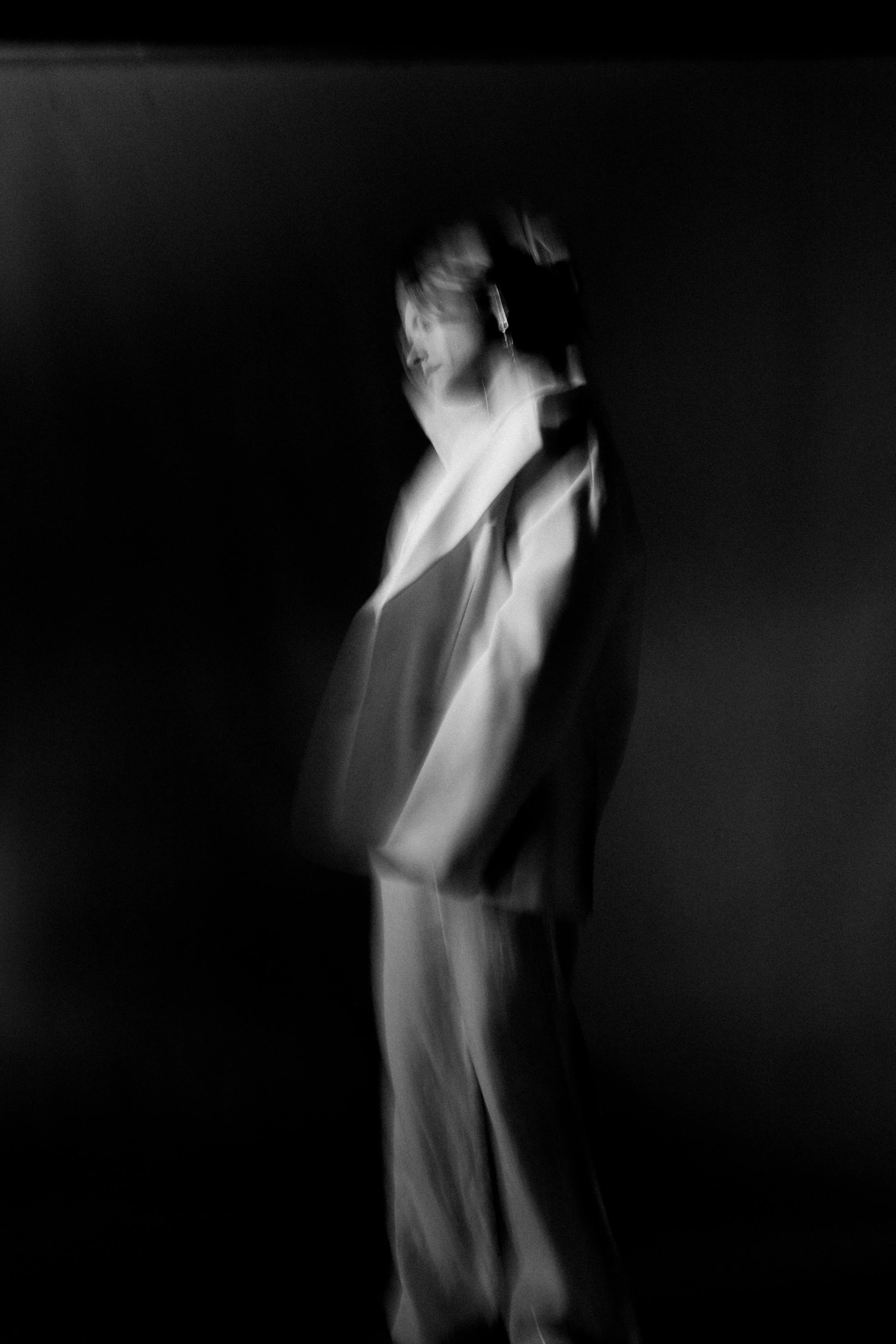 Imagem em preto e branco de uma pessoa em movimento, com efeito desfocado, usando roupa ampla e capuz.