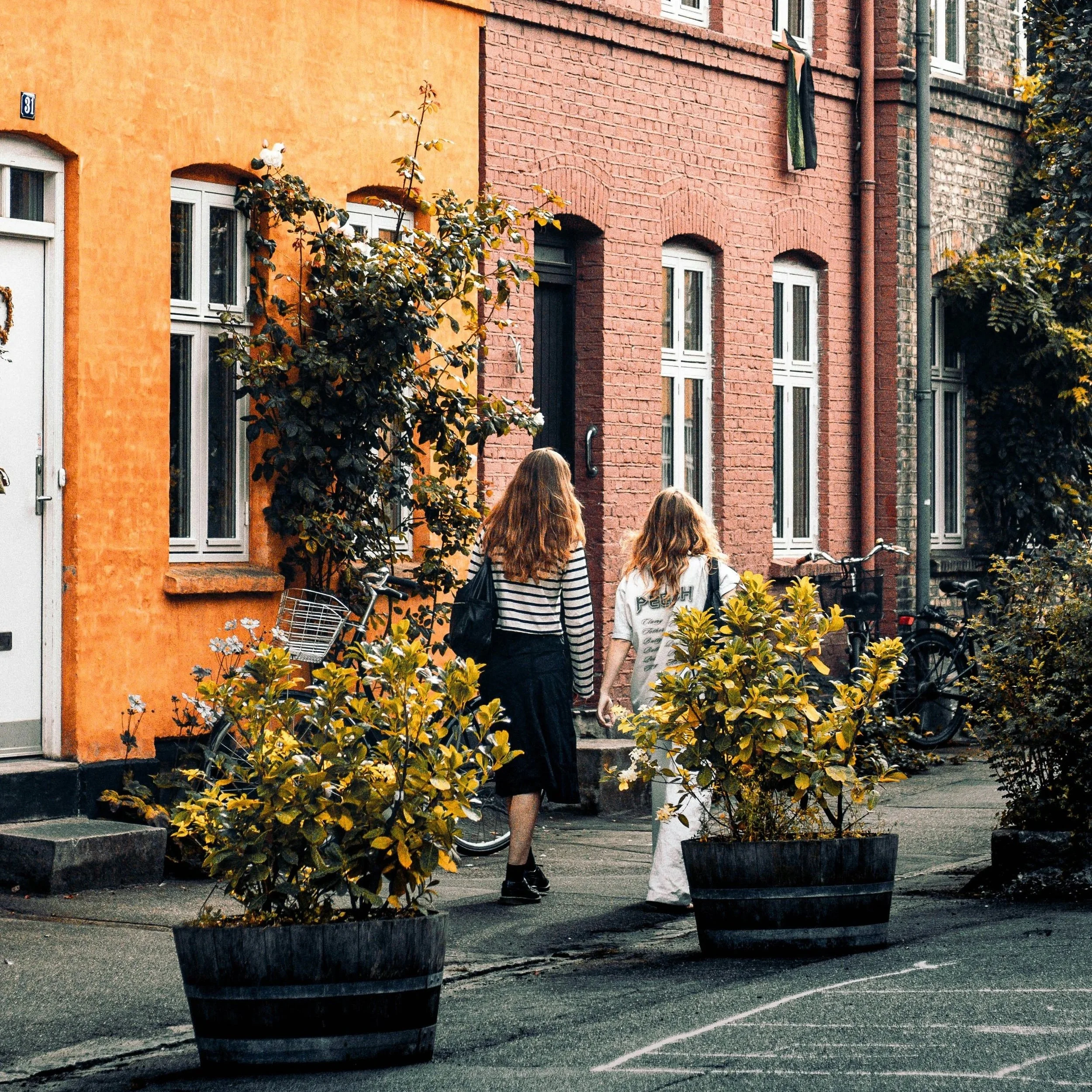 two young women walking on the sidewalk among colourful historic houses in Copenhagen.