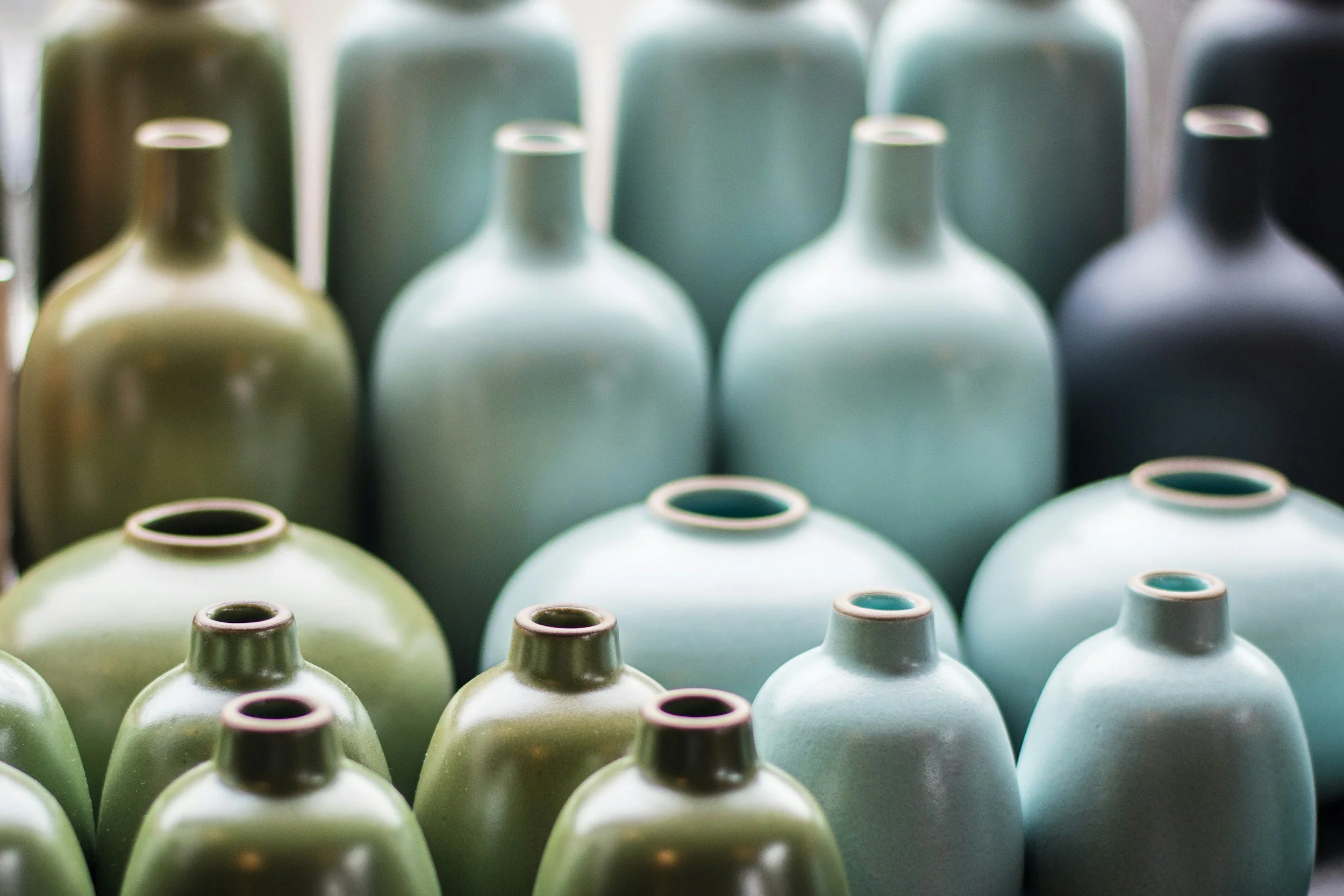 Multiple ceramic vases in shades of green, white, and black arranged in rows.