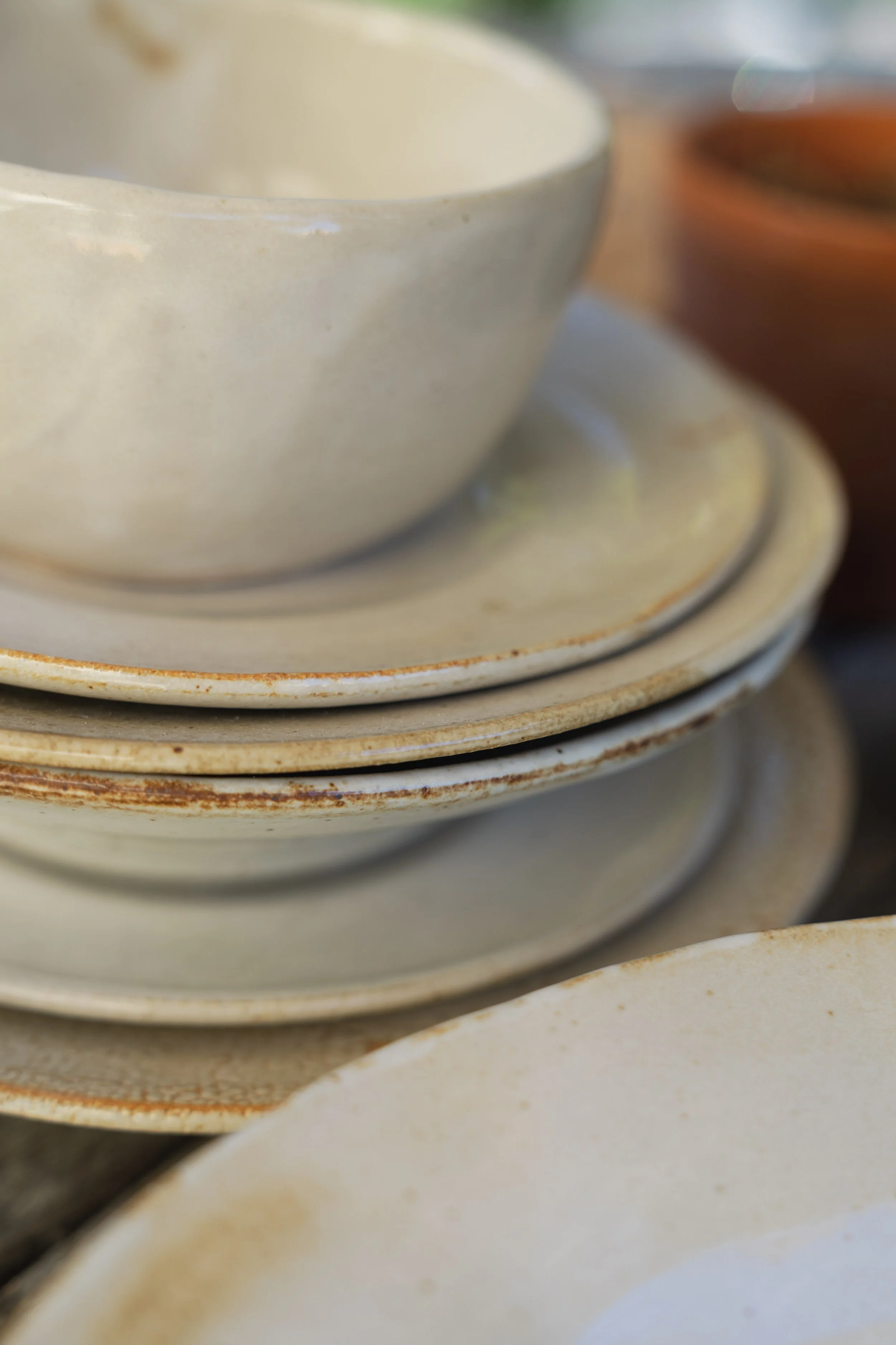 Stack of rustic, off-white ceramic plates and bowls with slightly chipped and worn edges.