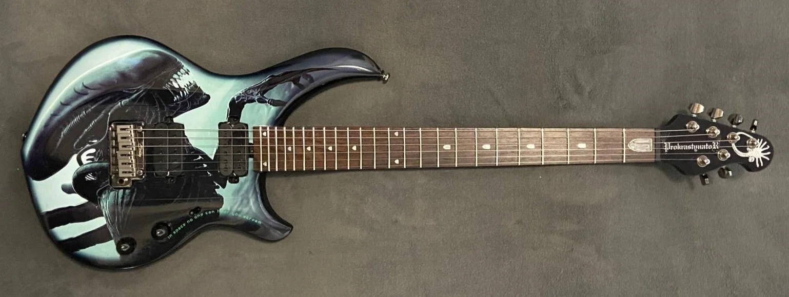 Electric guitar with a black, white, and green graphic design, mounted on a dark gray surface.