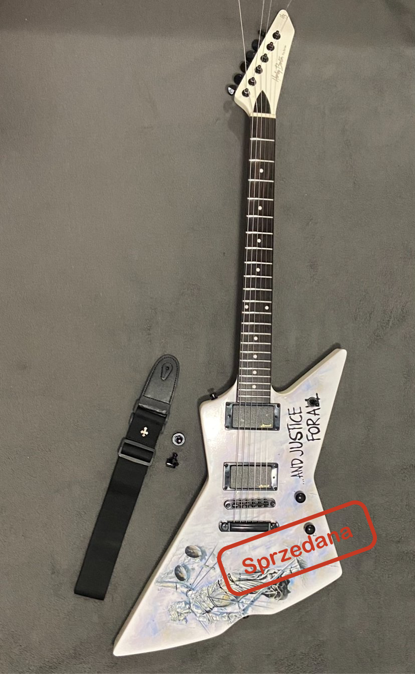 Electric guitar with a white body, black neck, and headstock, featuring handwritten text that says 'AND JUSTICE FOR ALL' and a red stamp that says 'Sprzedana', along with a black strap, a tuning key, and a small screw.