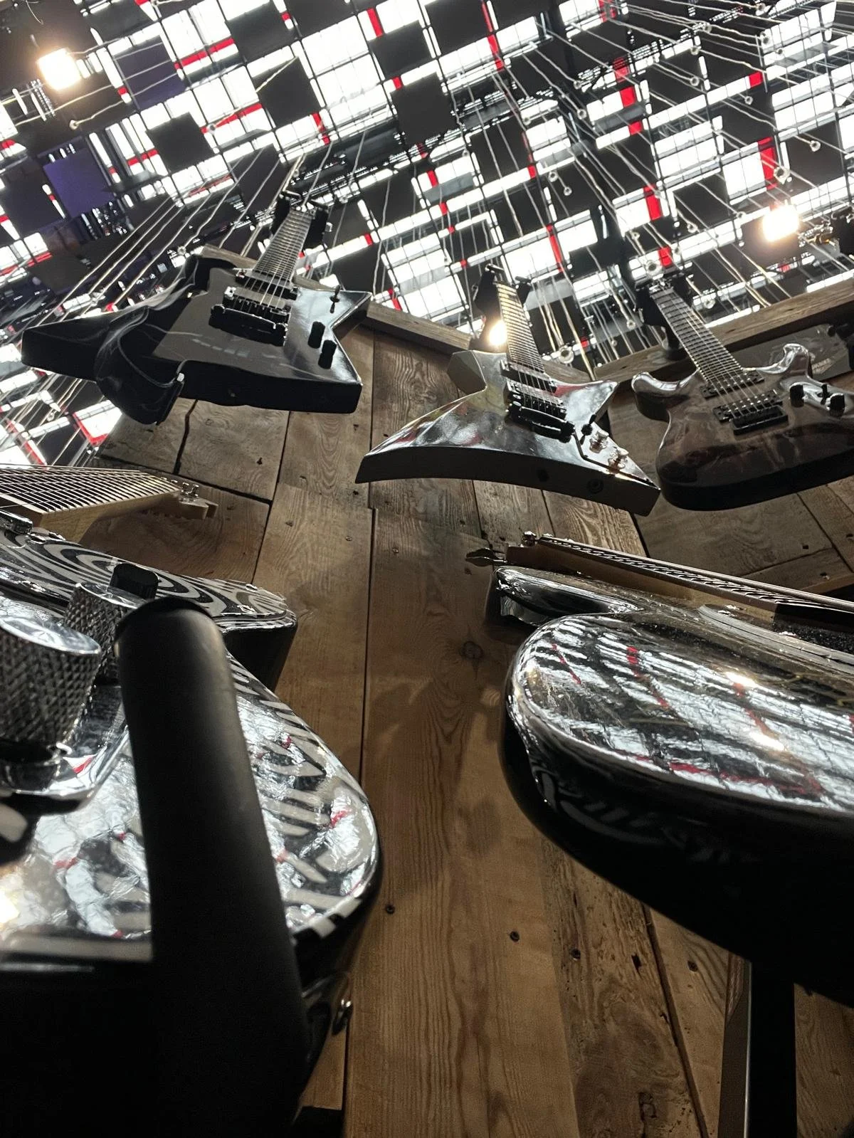 Several electric guitars hanging from the ceiling above a wooden wall in a room with an industrial-style ceiling grid