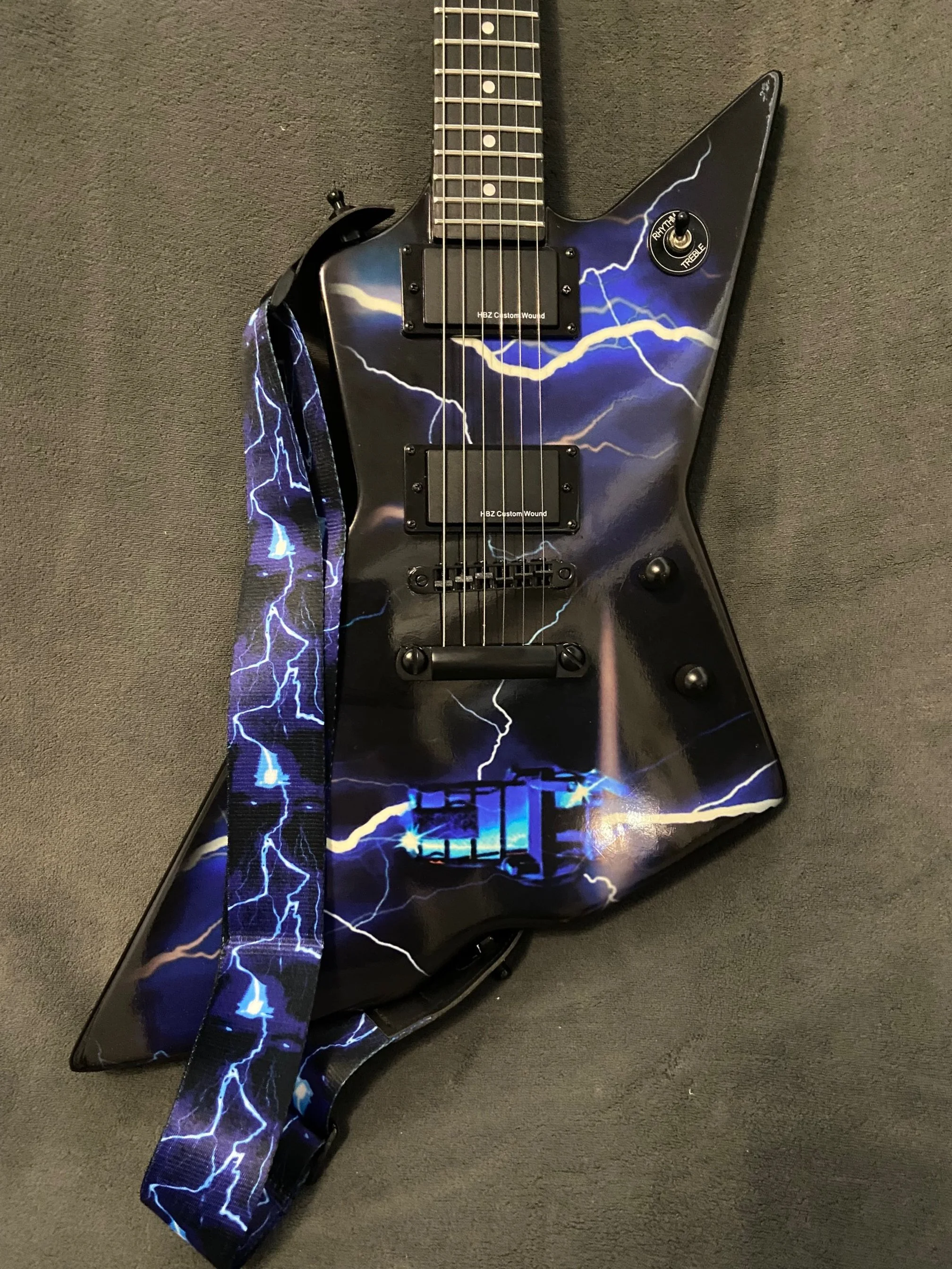 Electric guitar with a lightning storm design, black body, and a lightning strap.