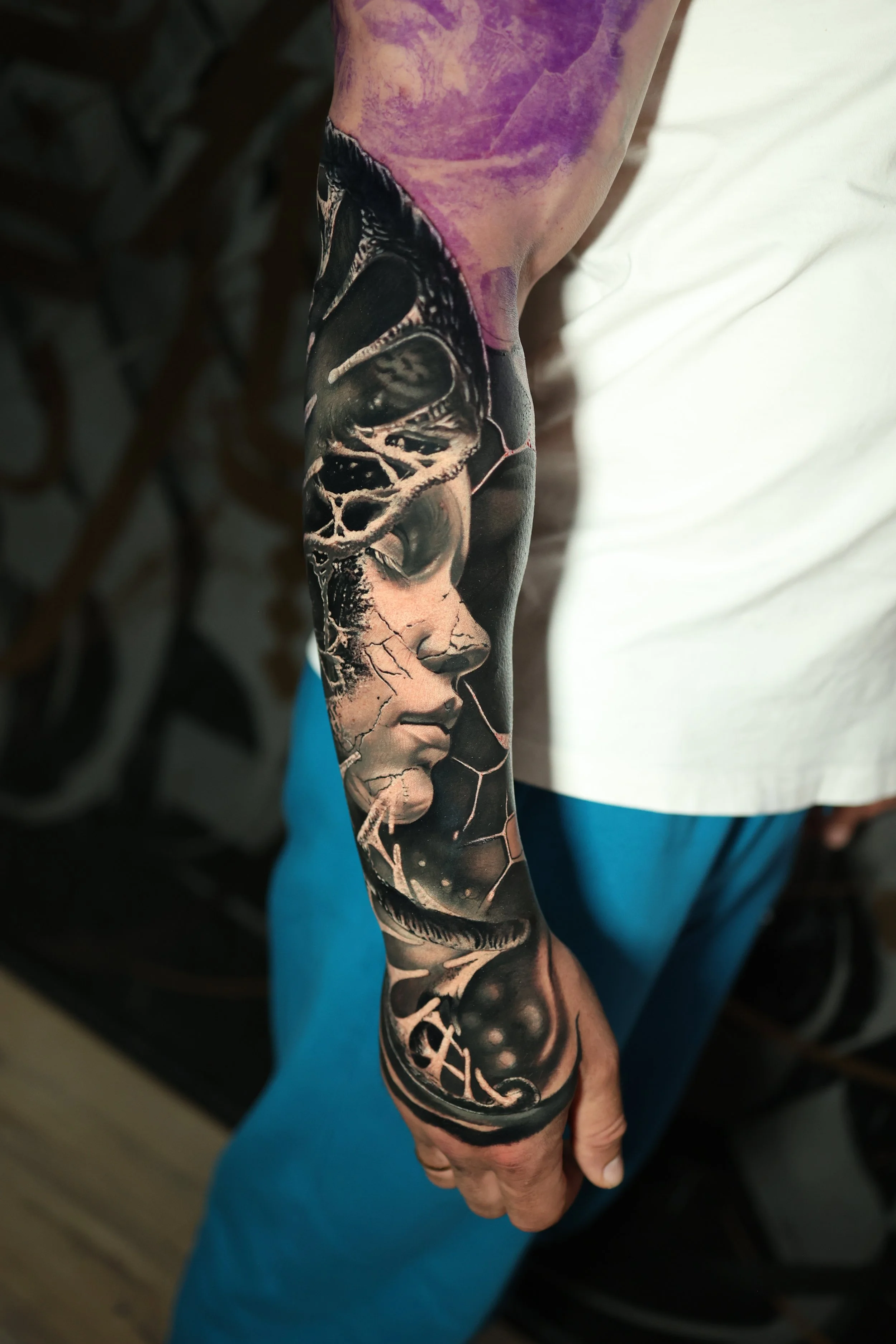 A person's arm with a detailed black and gray tattoo featuring a woman's face with closed eyes, flowing hair, and butterfly wings, extending from the shoulder to the wrist.