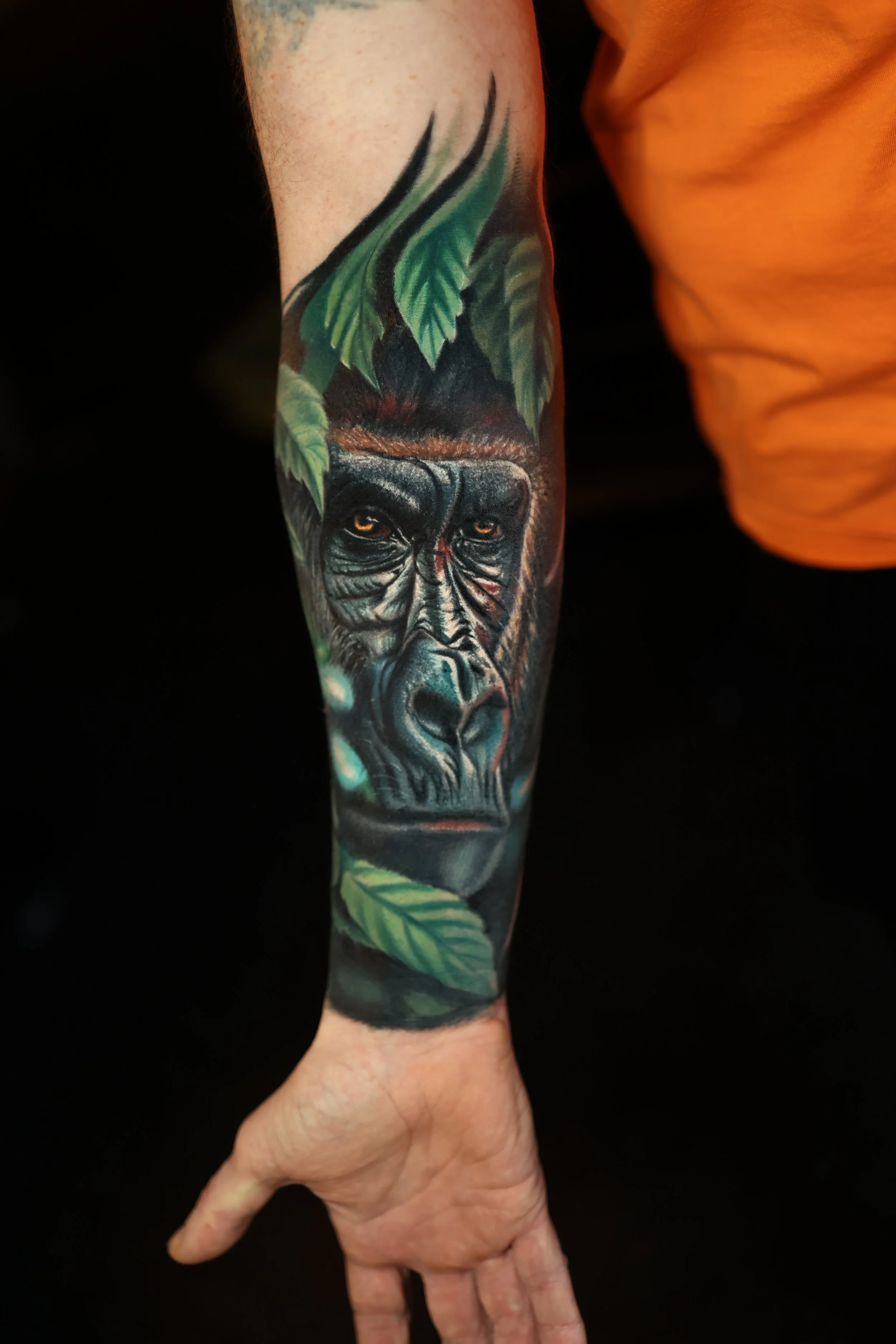 A person's forearm with a detailed tattoo of a gorilla's face surrounded by green leaves.