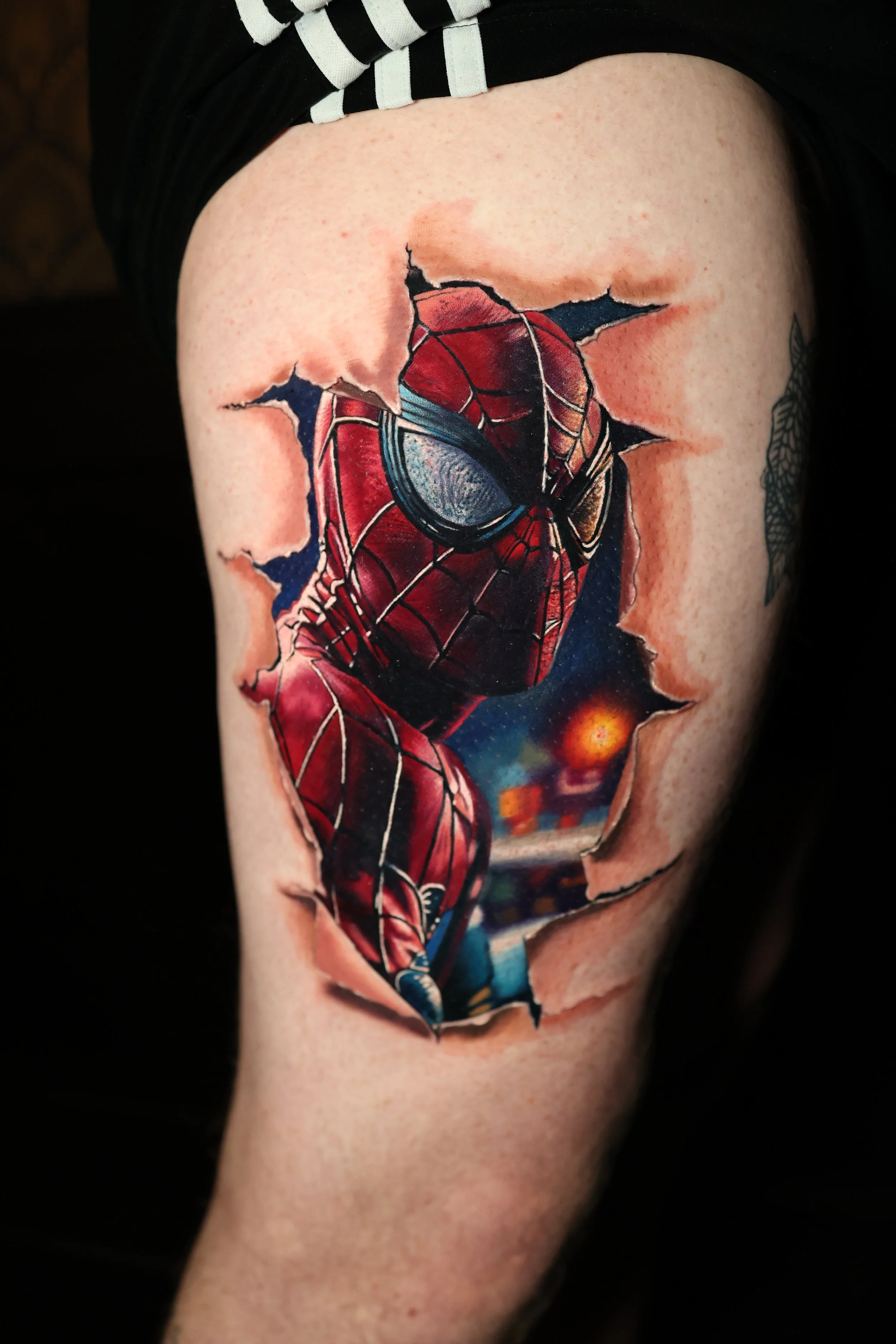 A tattoo of Spider-Man appears as if it is tearing through the skin, revealing a cosmic background with stars and planets.