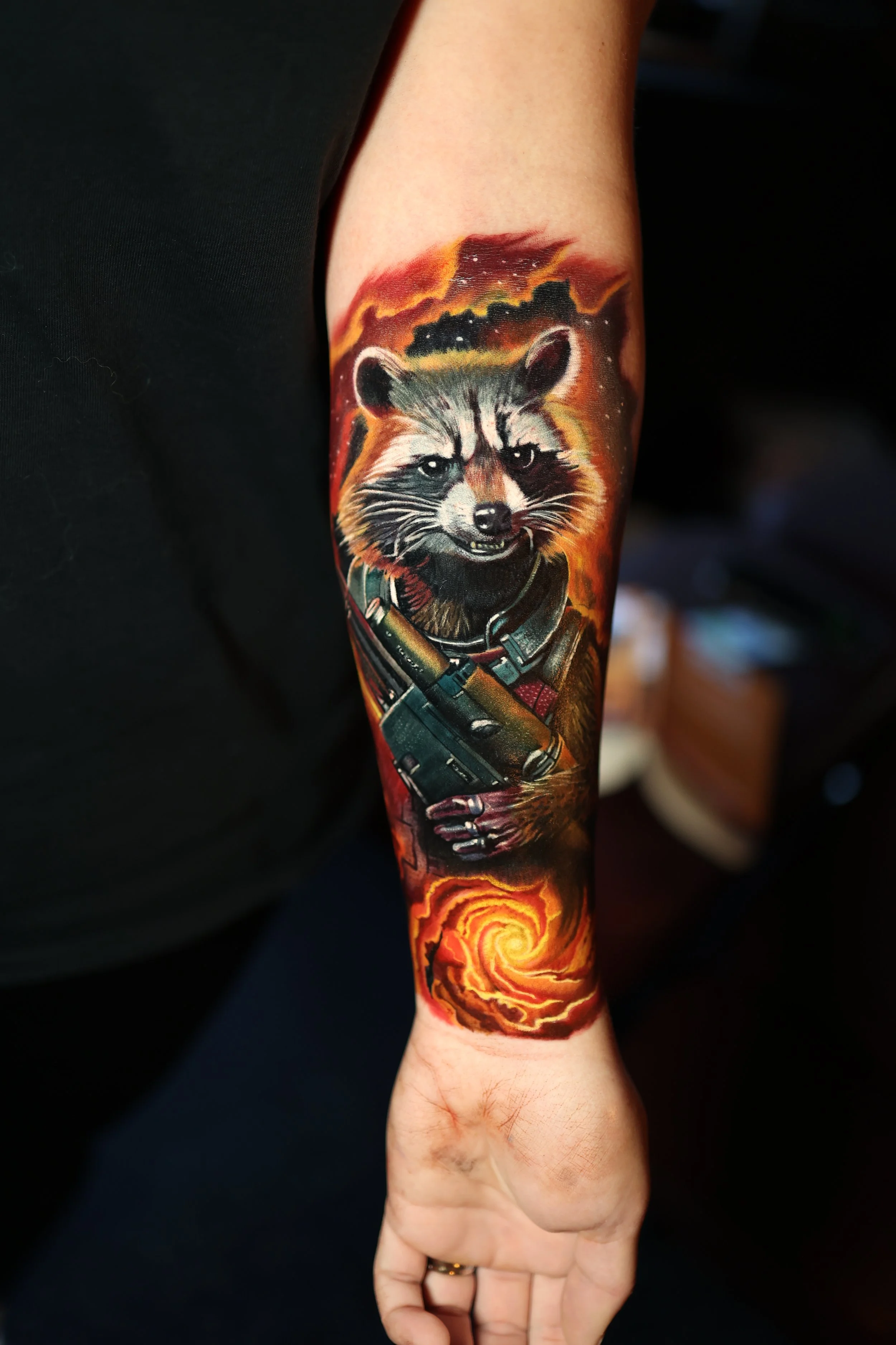 Tattoo of a raccoon with a fiery background, holding a weapon, on a person's arm.