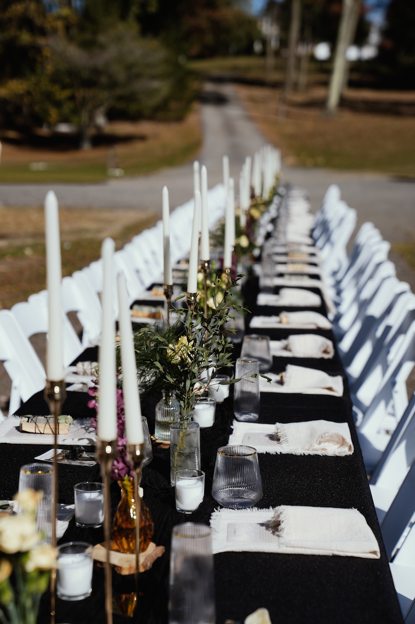 White Paddded Chairs around a rectangular tables with black table cloth set up for a meal