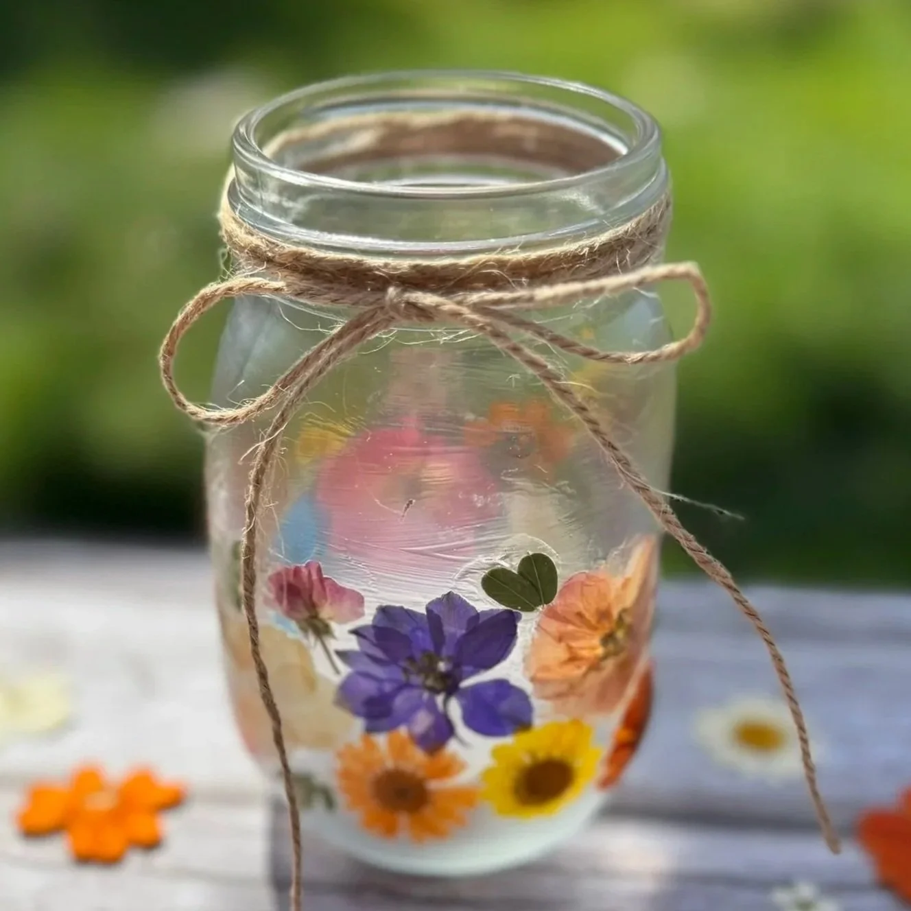 A pressed flower lantern made with a glass jar decoupaged with colorful pressed flowers and tied with a piece of twine.