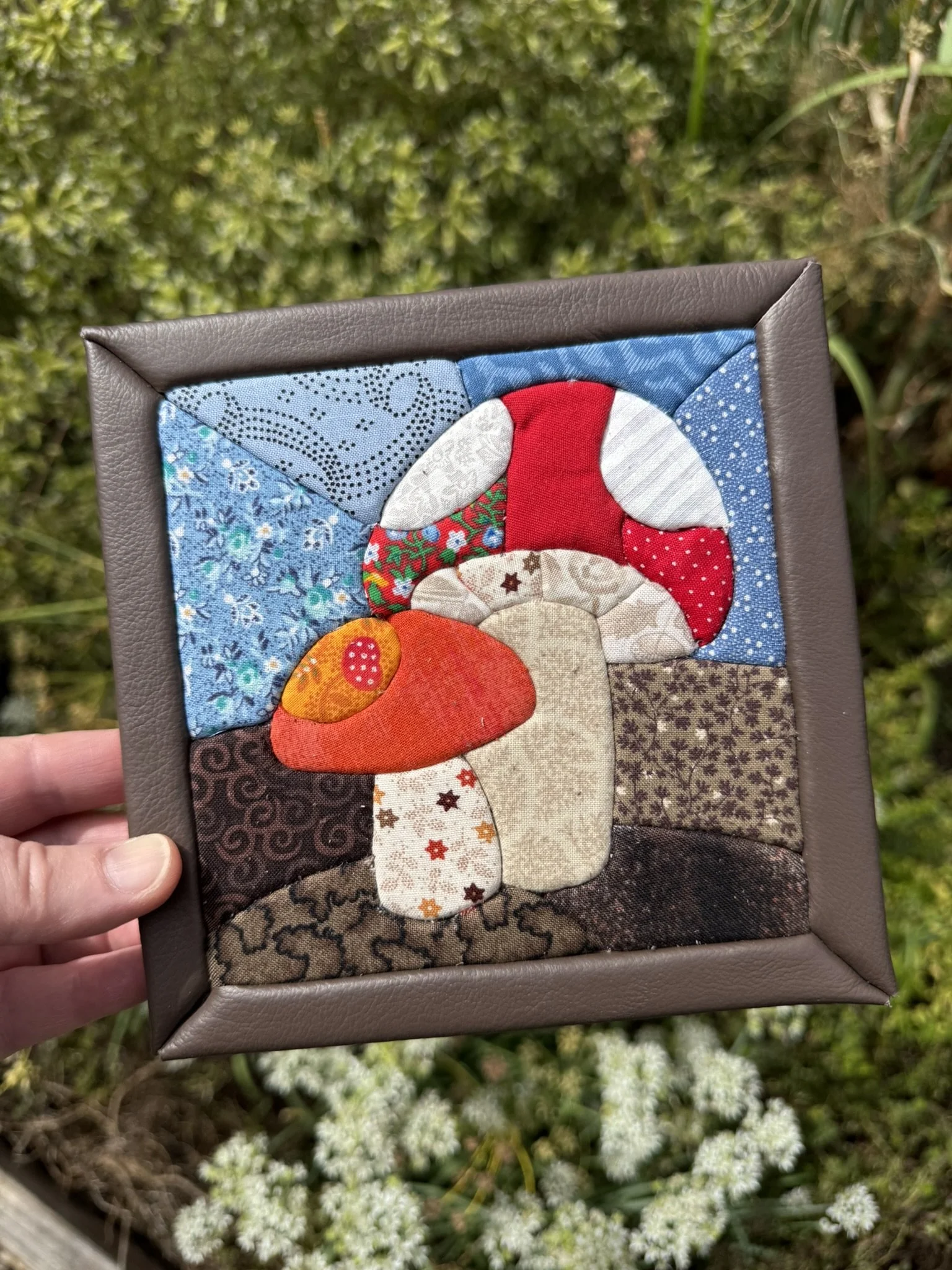 A kinusaiga artwork depicting a pair of mushrooms in red and orange with cream colored stems. They're on a brown and blue background with a brown leather frame.