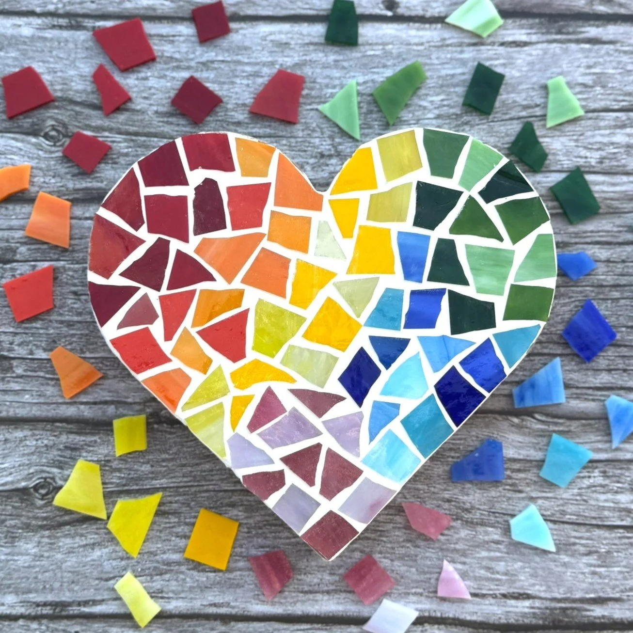 A small tray with a mosaic of colorful glass pieces in red, orange, yellow, green, blue, and pink, placed on a textured surface outdoors.
